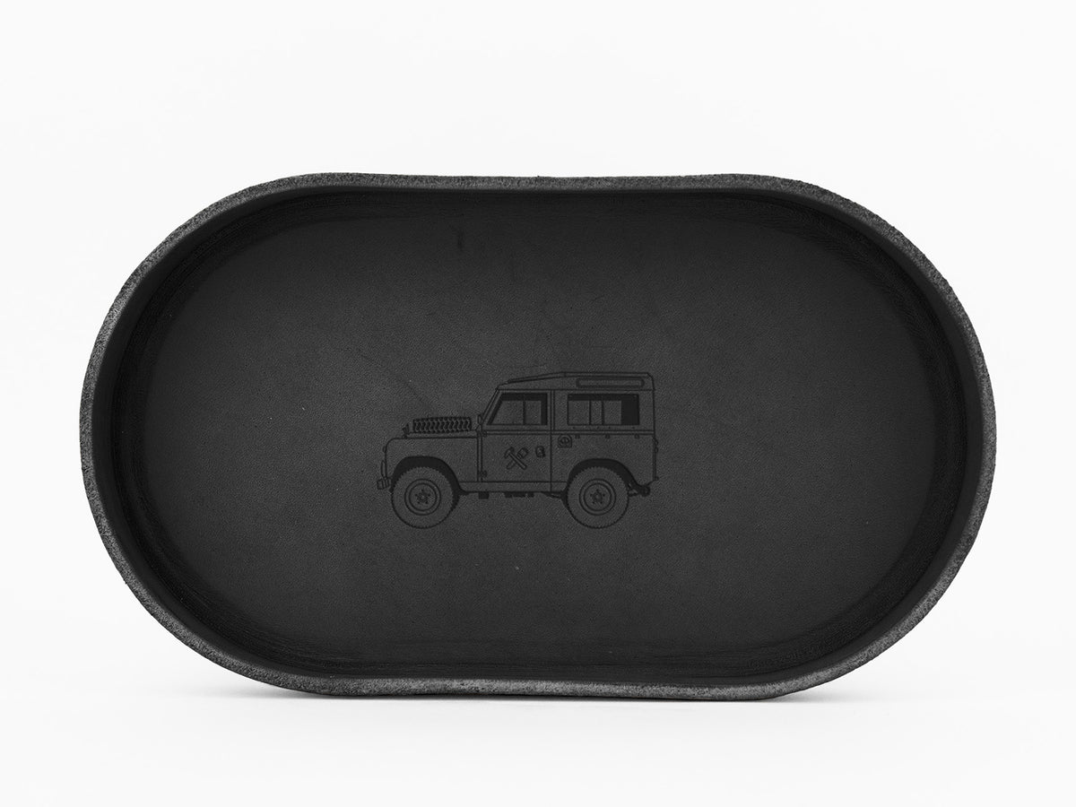 A black oval tray with a simple outline drawing of a classic off-road vehicle in the center, shown from a top-down perspective on a white background.