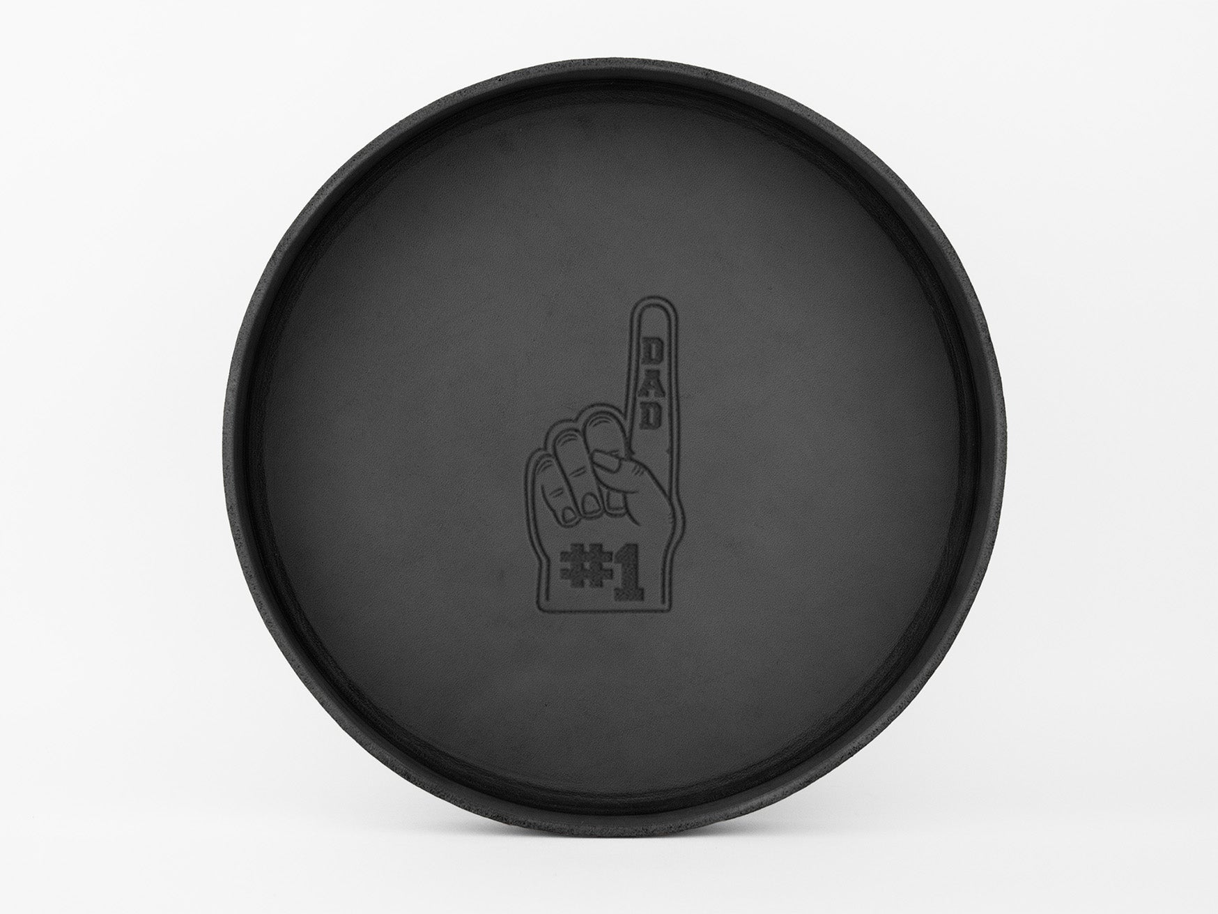 A round, black tray with an image of a foam finger printed in the center, showing the index finger raised and the words “DAD #1” written on it. The background is plain white.
