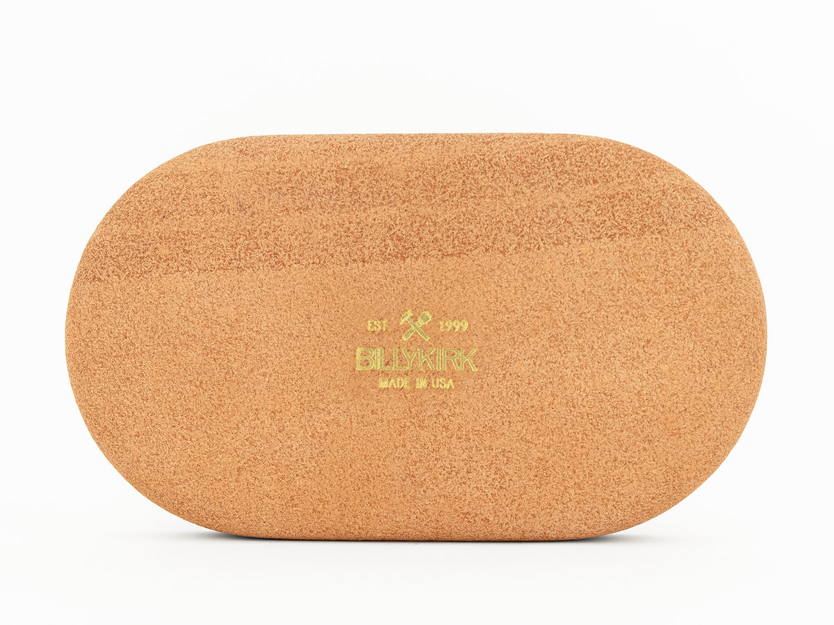 The back of an oval-shaped, natural colored leather tray with Billykirk MADE IN USA and a crossed hammer and maul logo printed in gold foil on the back, placed against a white background.