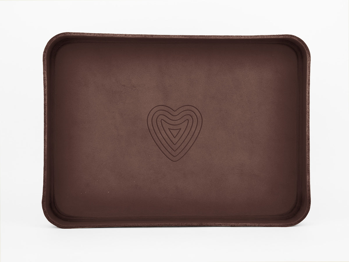 A rectangular brown tray with curved edges, featuring a simple, embossed heart-shaped design with multiple outlines at the center. The tray is set against a plain white background.