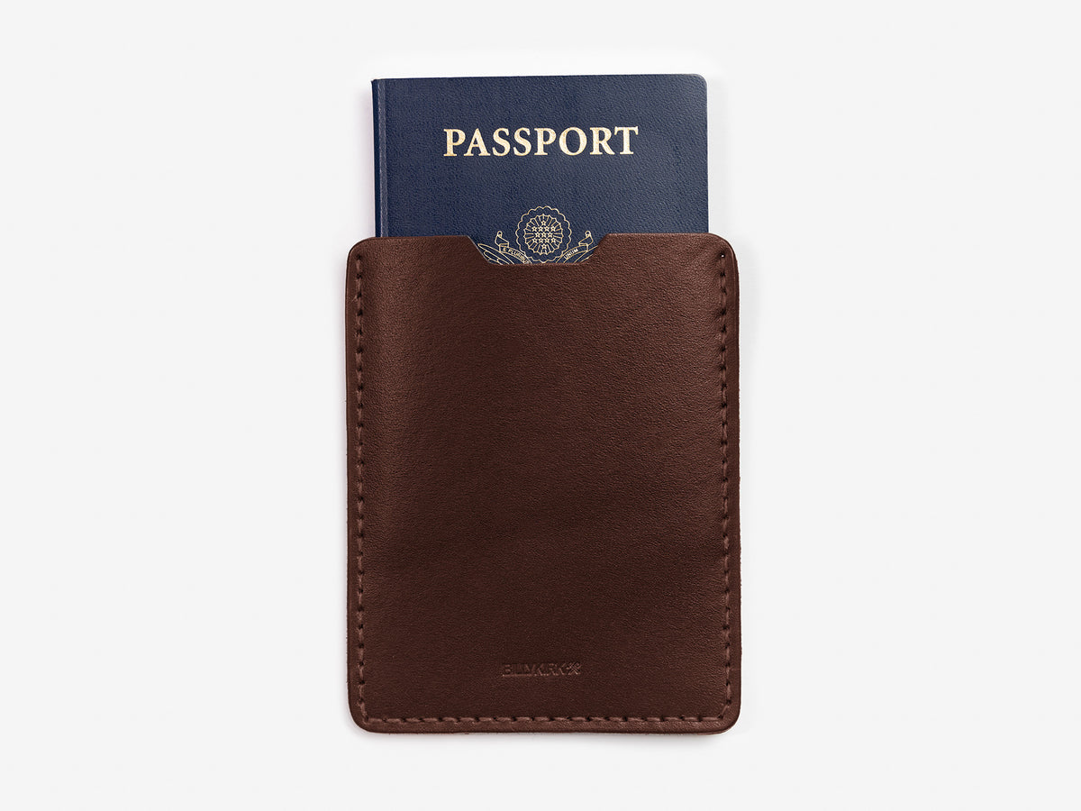 A blue passport partially tucked into a brown leather sleeve against a white background.