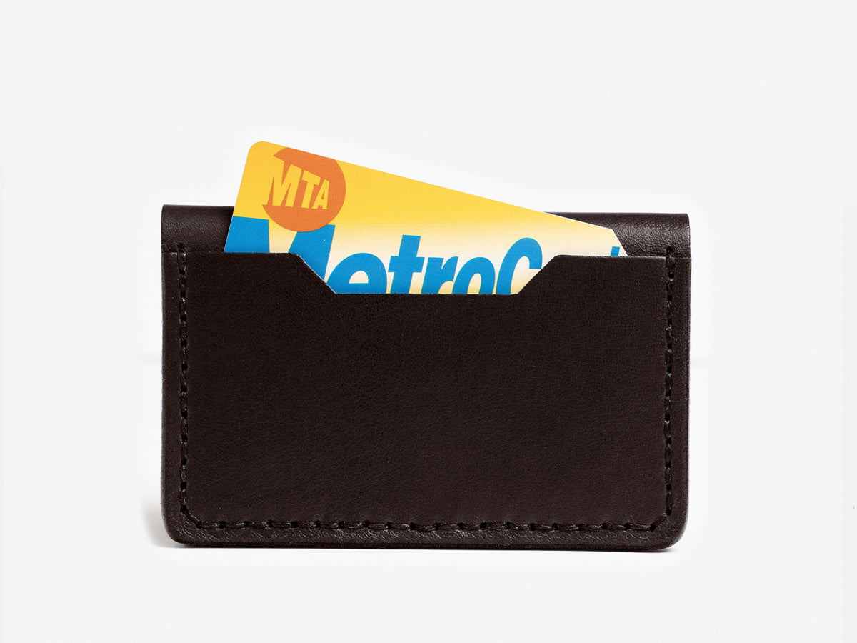 A black leather card holder with an MTA MetroCard partially visible inside, set against a plain white background.
