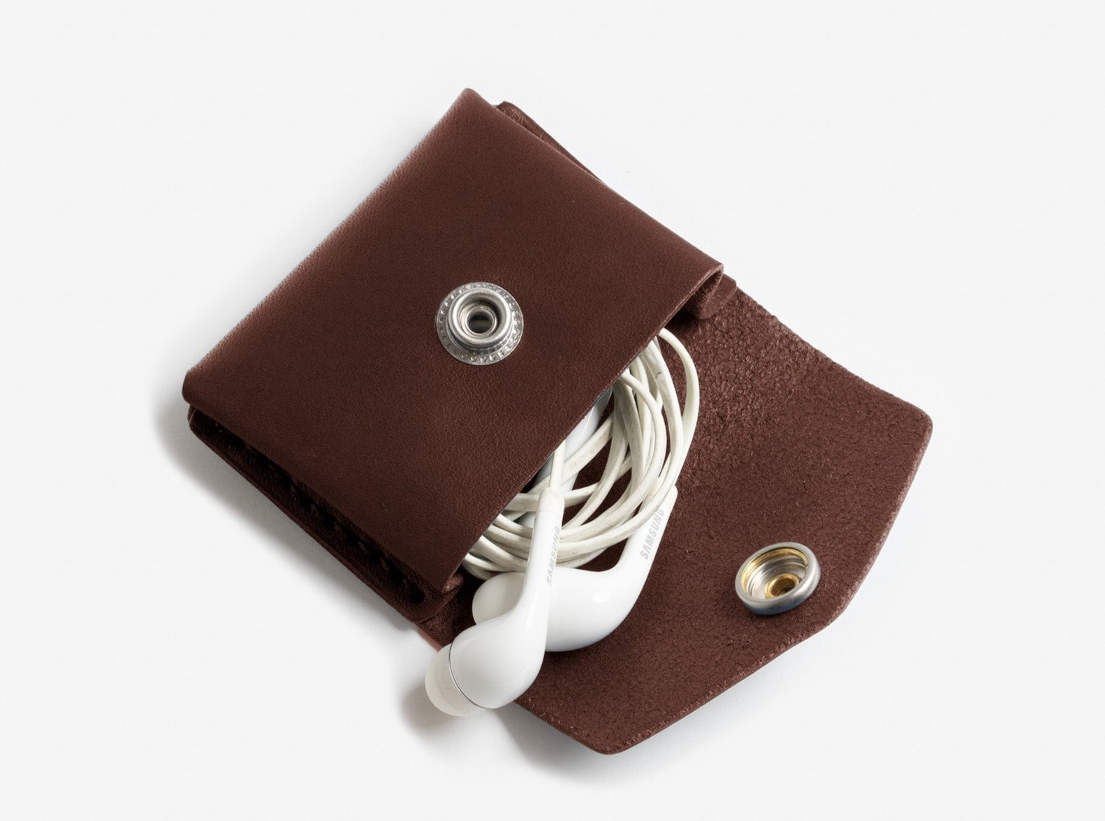 A hickory leather coin pouch with a nickel plated snap closure, displayed with headphones inside.
