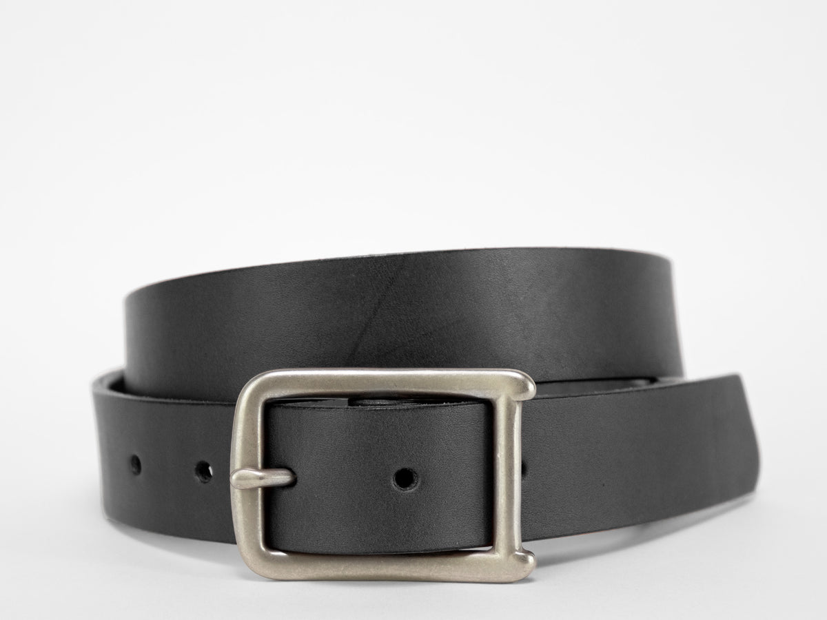 A black leather belt with a silver rectangular buckle is coiled on a plain white background.