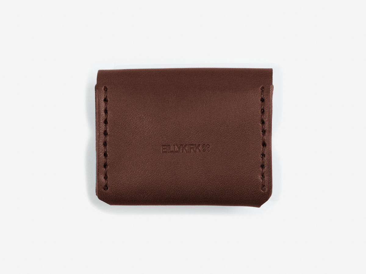 The back of a tan coin pouch with hand-stitched edges with a Billykirk logo embossed in the center