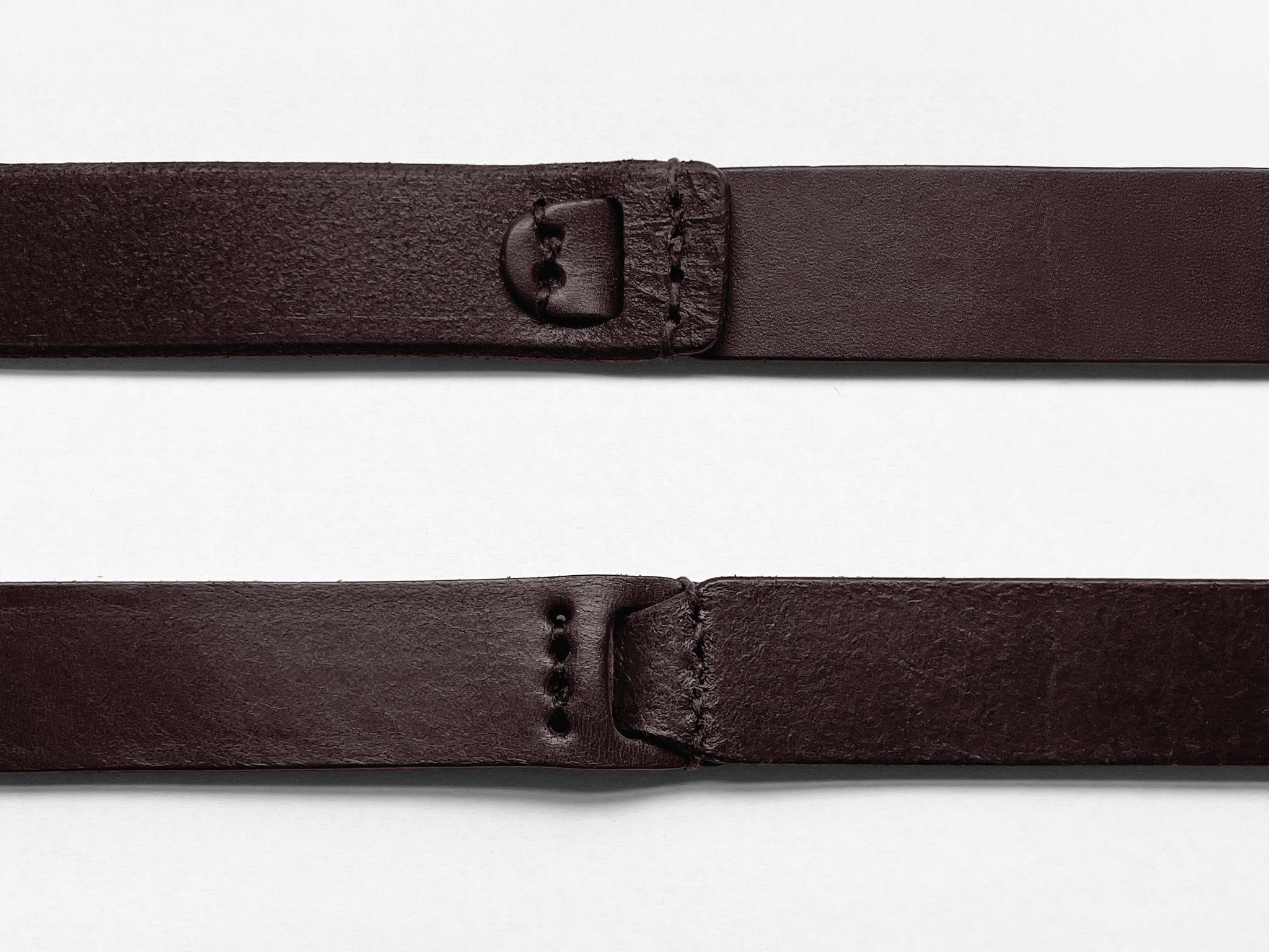 Close-up of two dark brown leather belt straps laid parallel on a white surface, showing stitching, holes, and buckle attachments, with one strap slightly curved at the end.