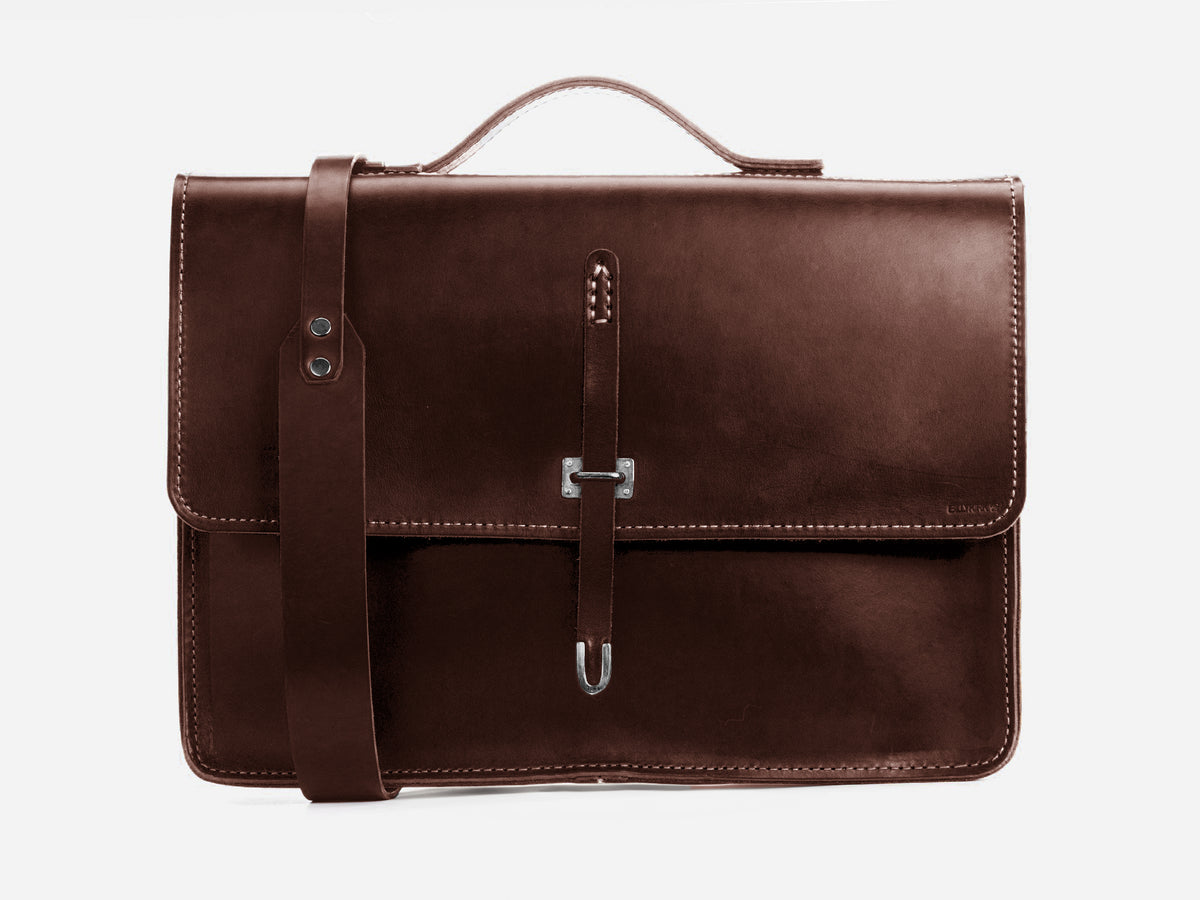 A brown leather briefcase with a front flap, silver buckle clasp, visible stitching, a top handle, and a matching leather shoulder strap, displayed against a plain white background.