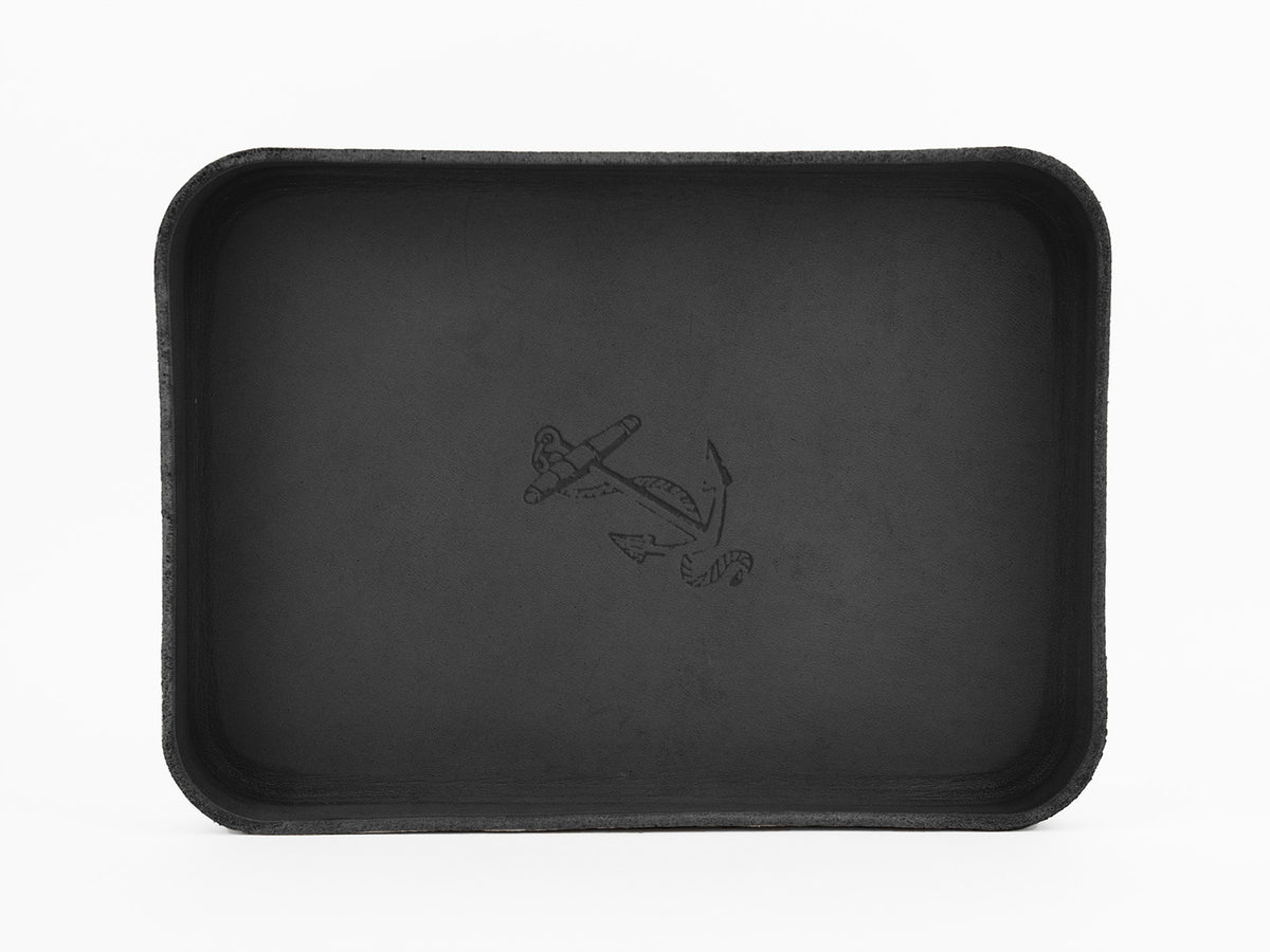 A rectangular black tray with rounded corners, featuring a simple anchor design etched in the center against a plain white background.