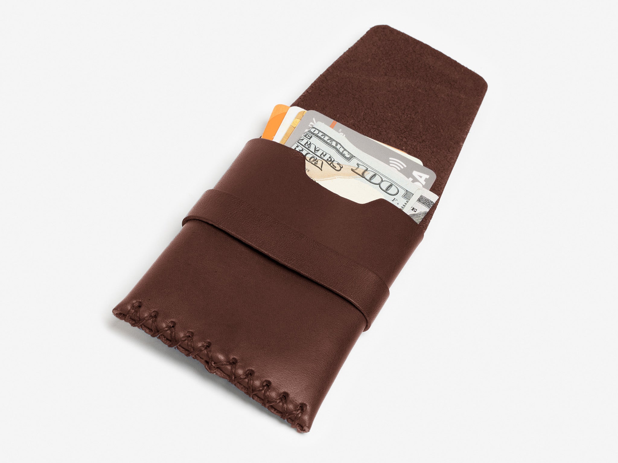 A brown leather wallet with visible stitching holds a folded hundred-dollar bill and two credit cards, partially sticking out, on a white background.