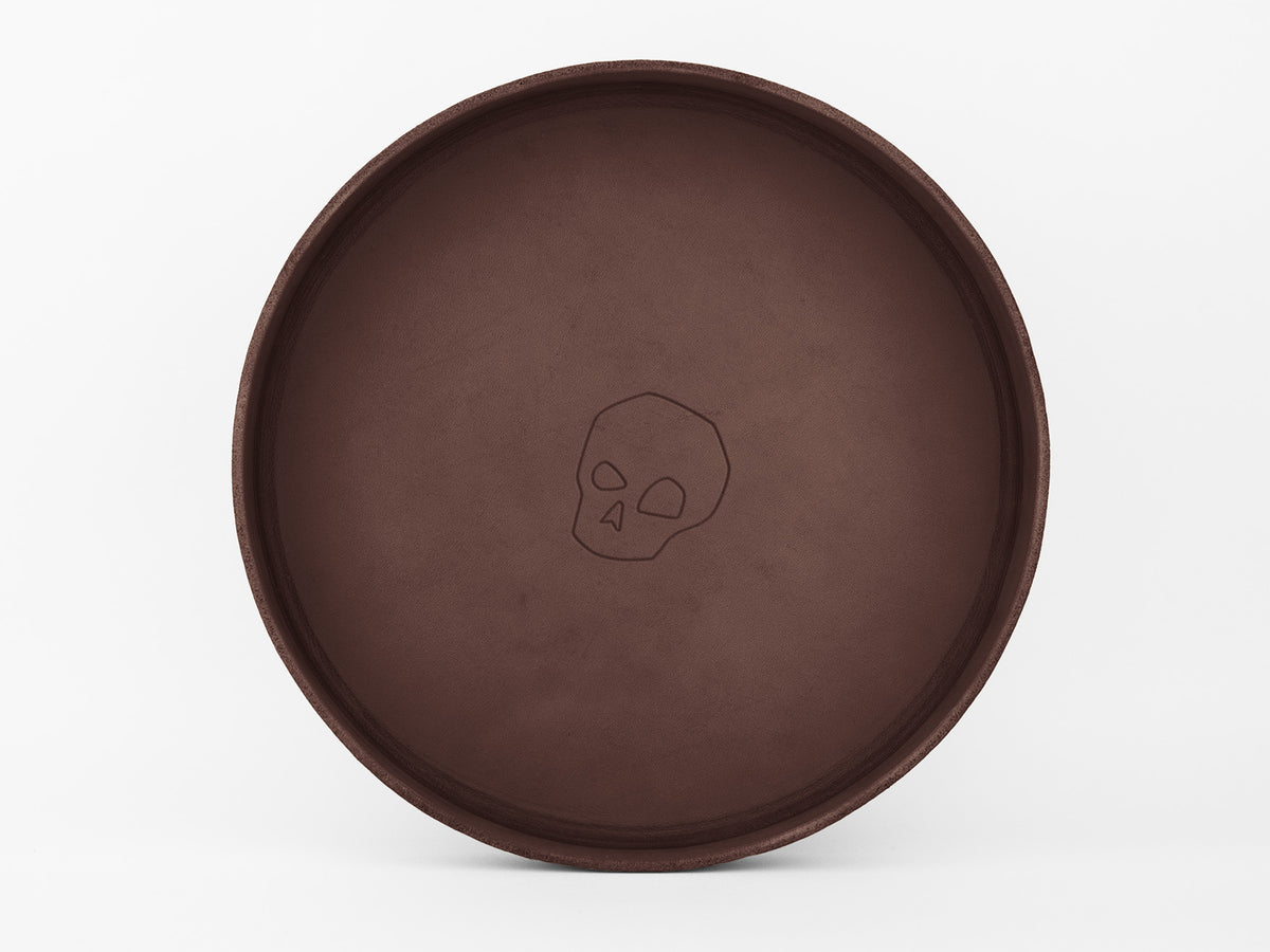 A round, brown tray with a simple outline of a skull design at the center, set against a plain white background.