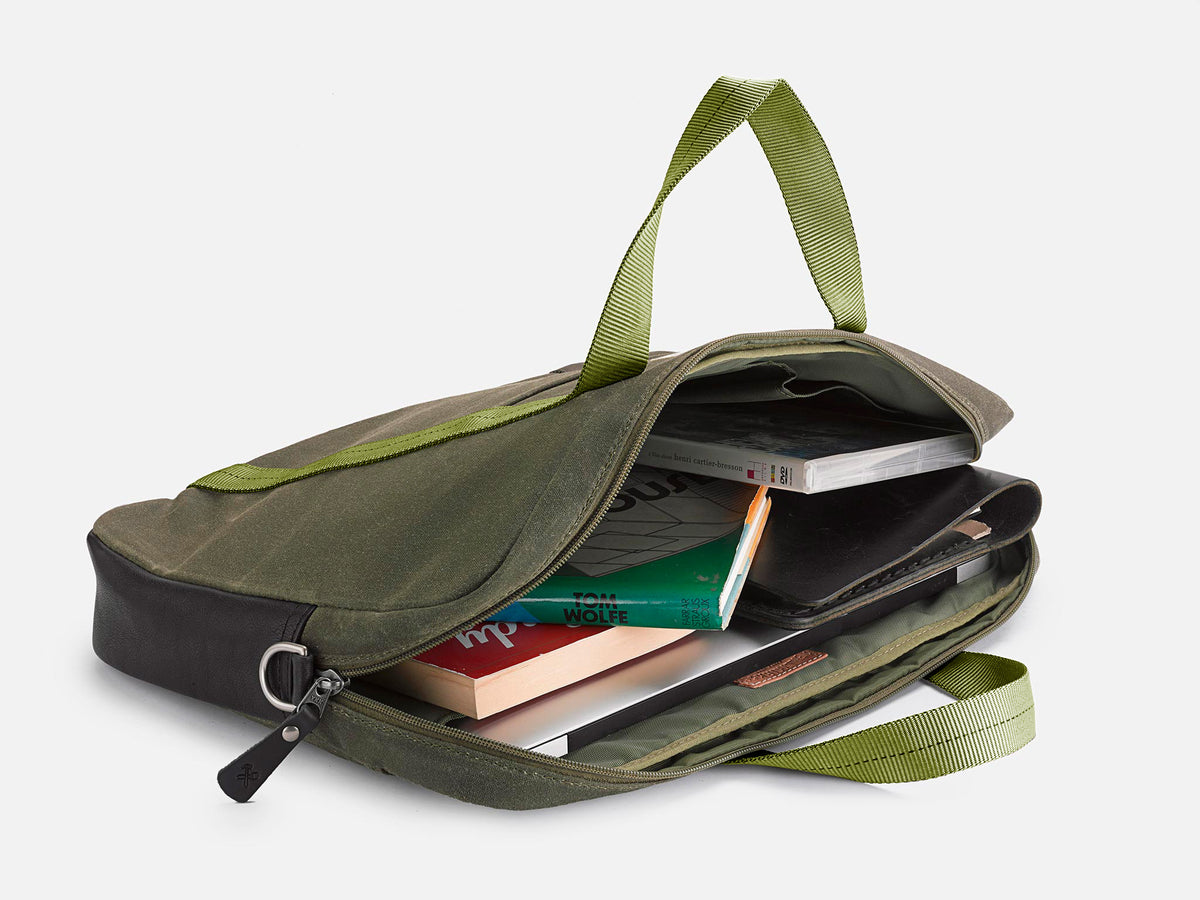 A green and black fabric bag, partially unzipped, with books, notebooks, and electronic devices visible inside. The bag has green carrying handles and is set against a plain white background.