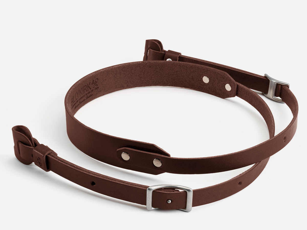 A brown leather rifle sling with silver metal buckles and rivets, displayed coiled on a white background.