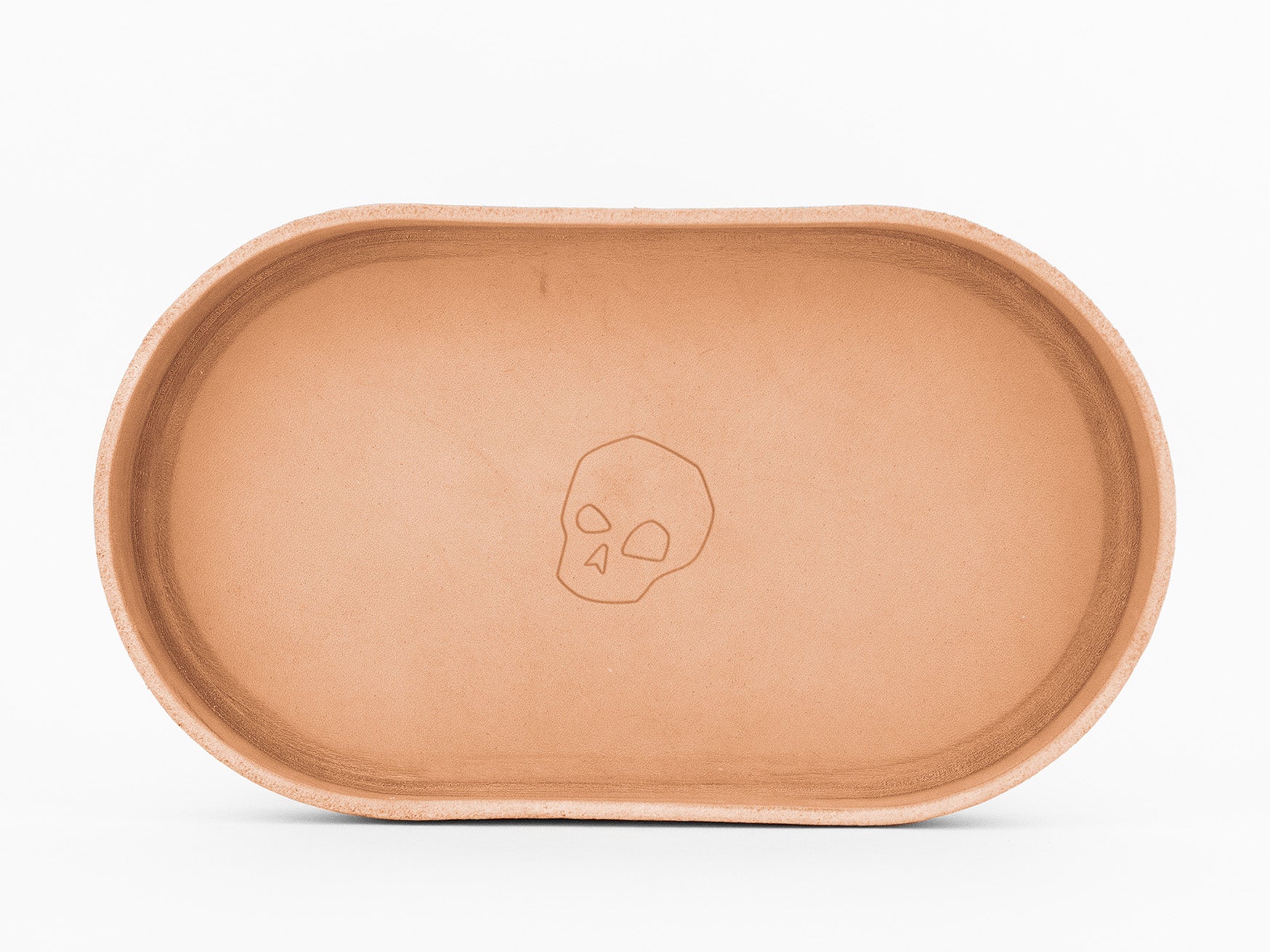 An oval-shaped, natural colored leather tray with a simple skull design engraved in the center, photographed against a white background.