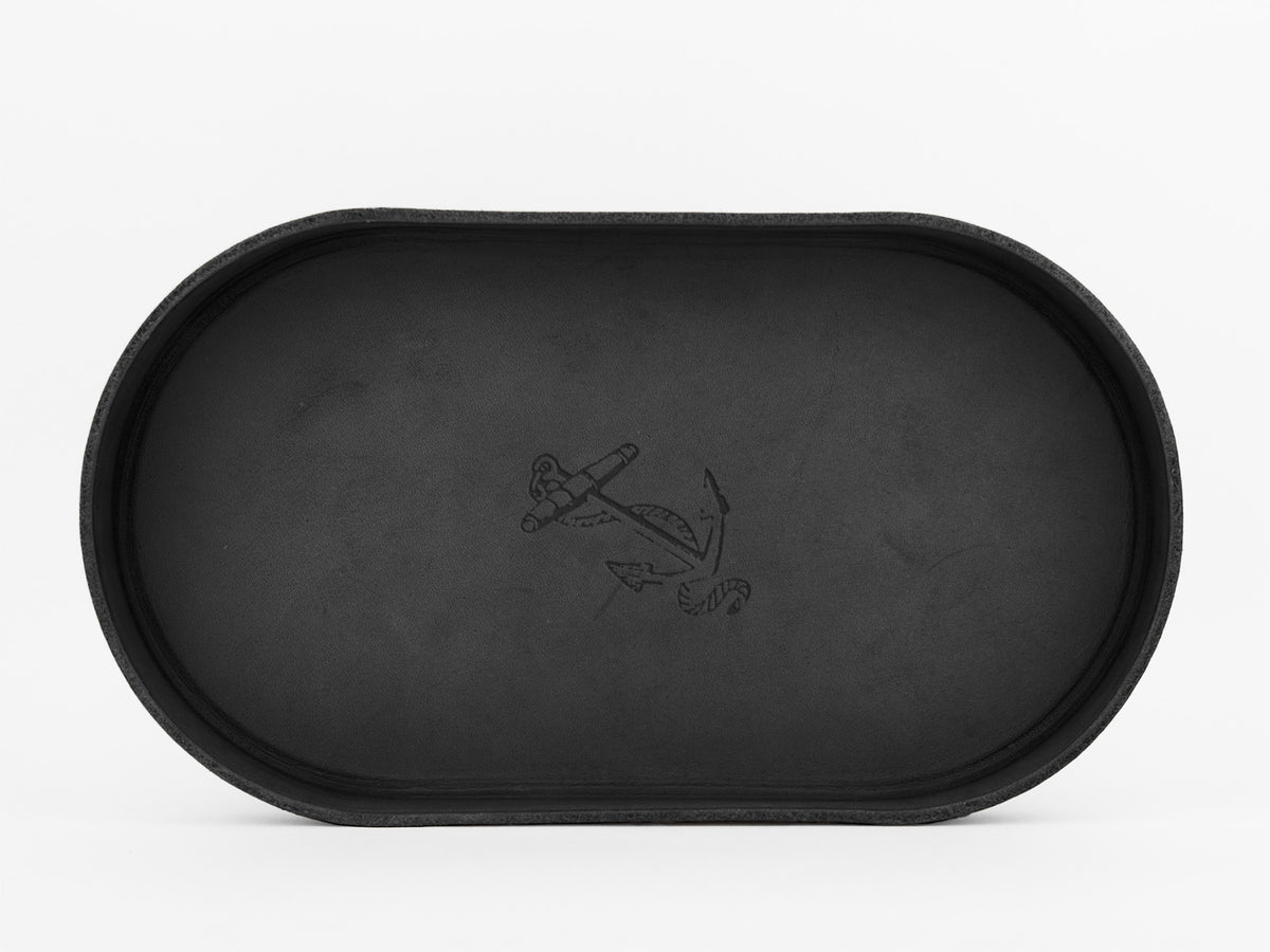 A black, oval-shaped tray with raised edges, featuring an anchor design etched in the center, set against a plain white background.