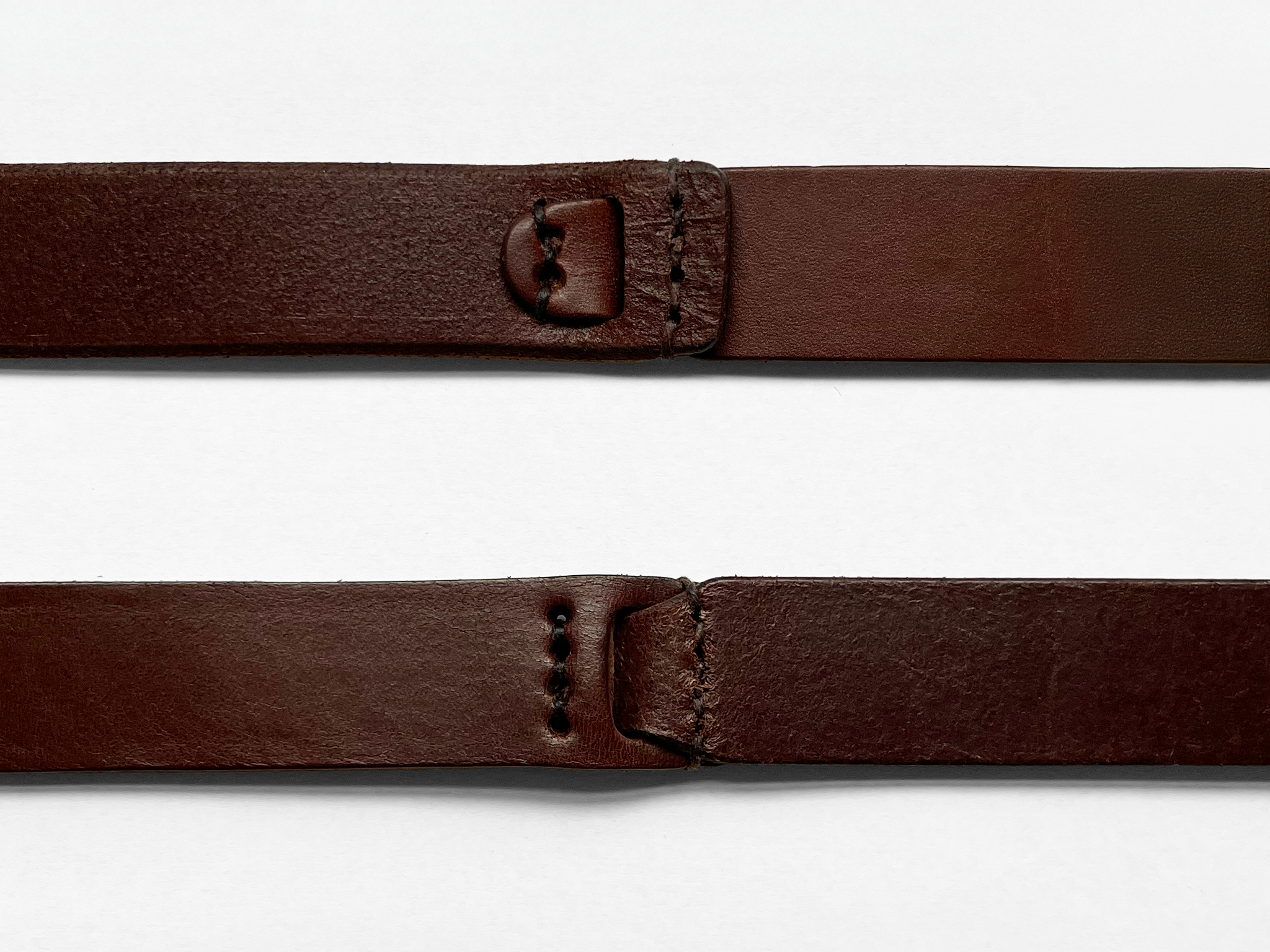Two brown leather straps are laid horizontally on a white background. Each strap has holes and stitching near the ends, showing different fastening options.