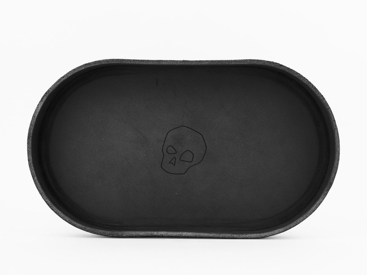 A black oval tray with a simple outline drawing of a skull in the center, placed on a white background.