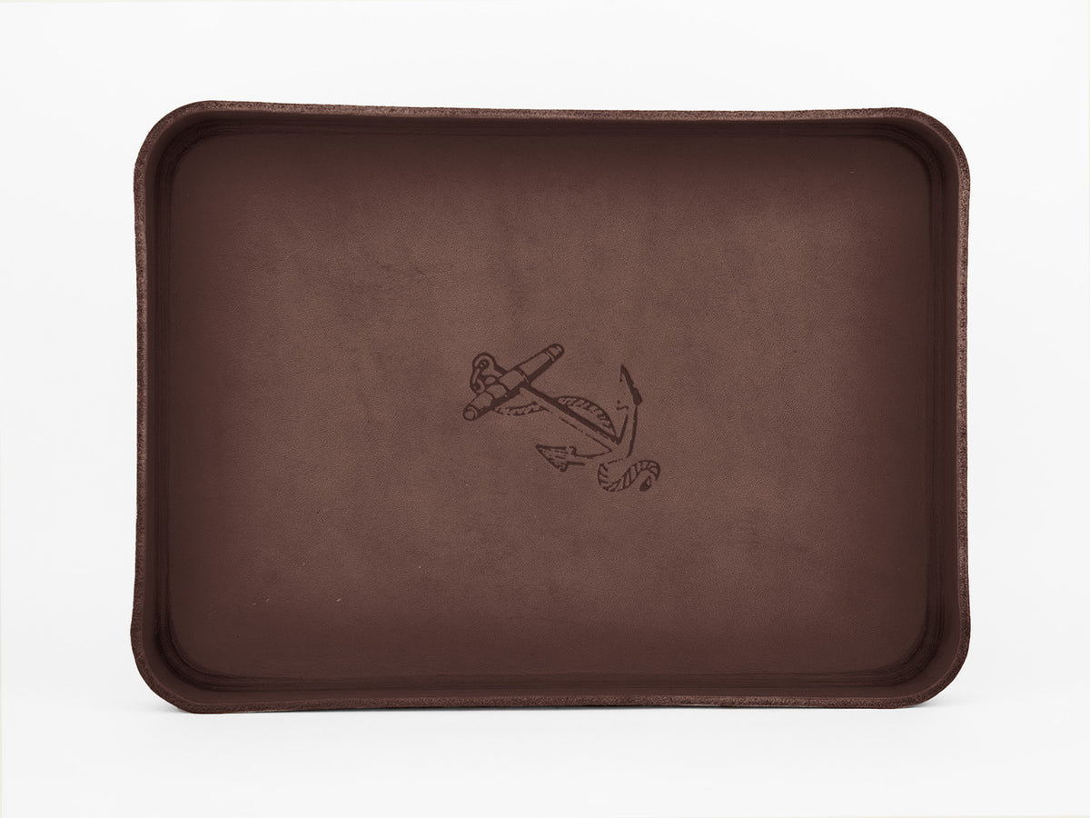 A rectangular brown tray with raised edges featuring a simple anchor and rope illustration engraved in the center. The background is plain white.