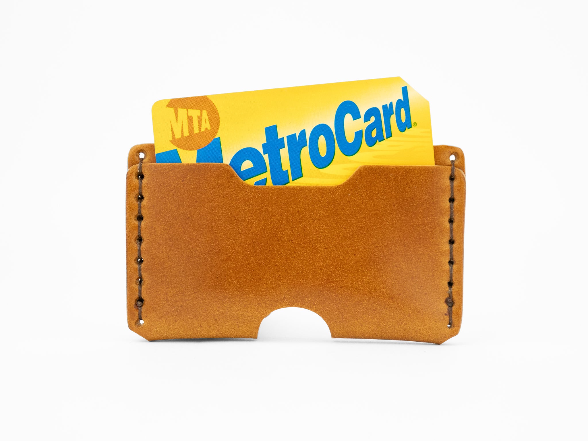 A tan cordovan leather card holder with a yellow and blue MTA MetroCard partially visible inside.