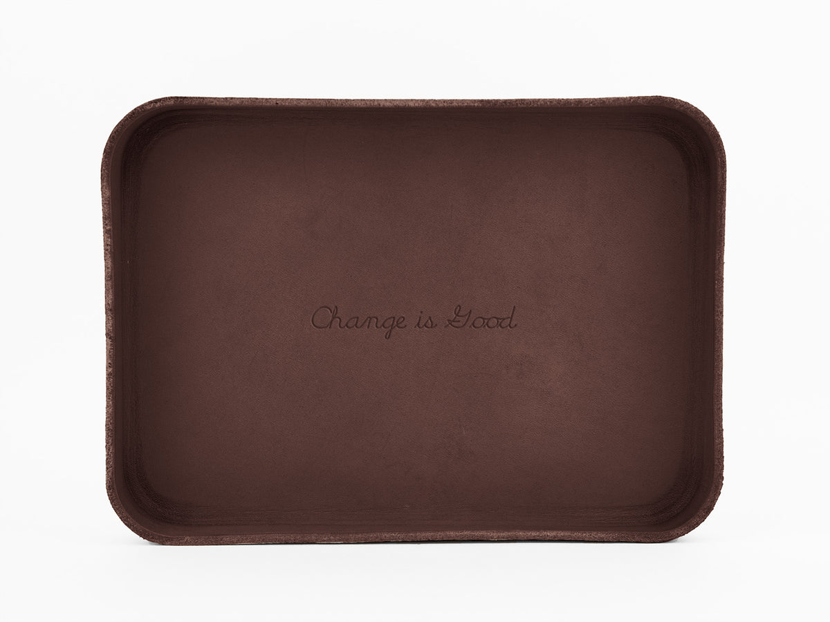A brown rectangular tray with rounded corners displays the phrase Change is Good engraved in the center. The background is plain white.