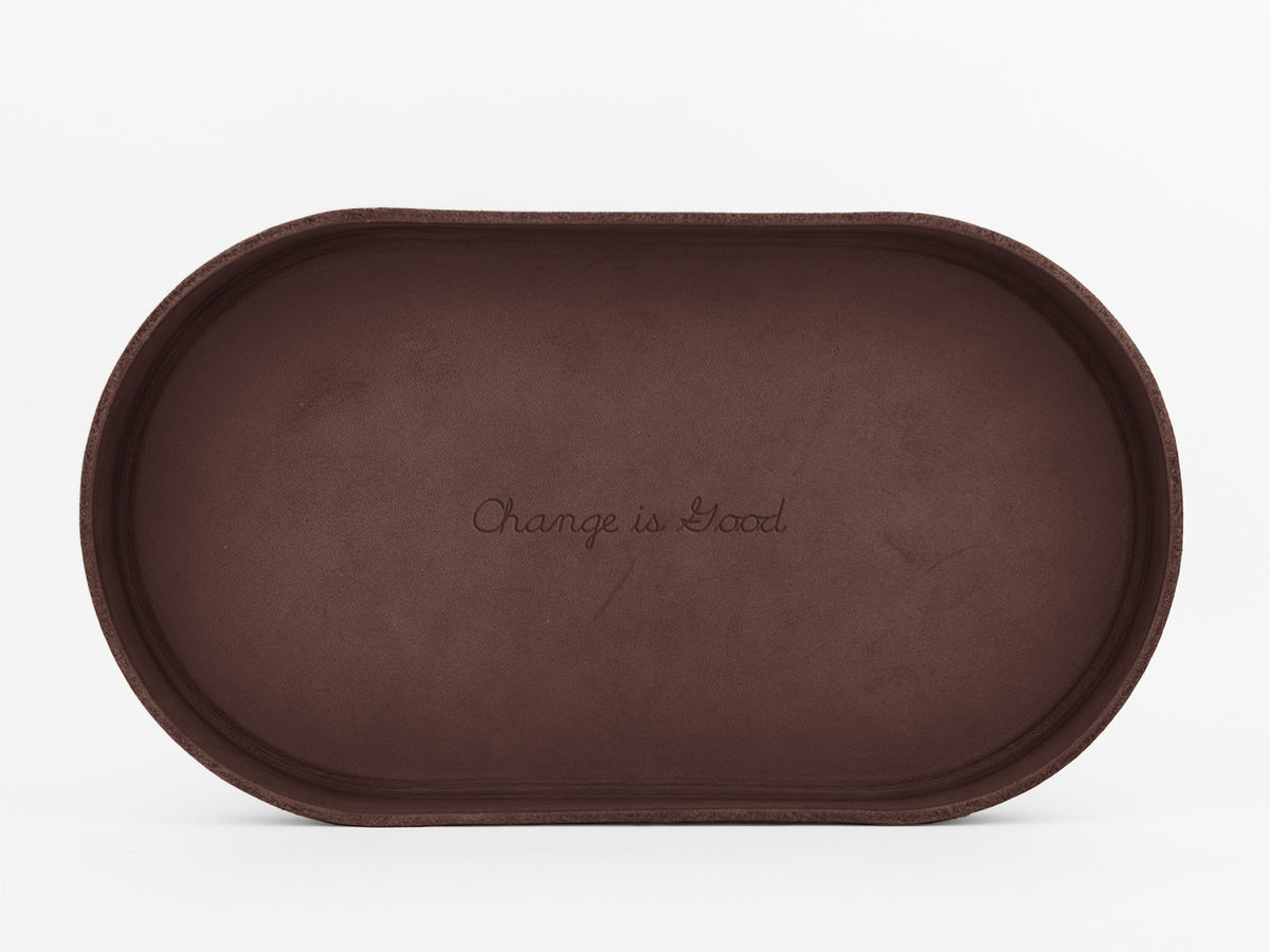 A brown, oval-shaped tray with the phrase Change is Good engraved in cursive at the center, set against a plain white background.

