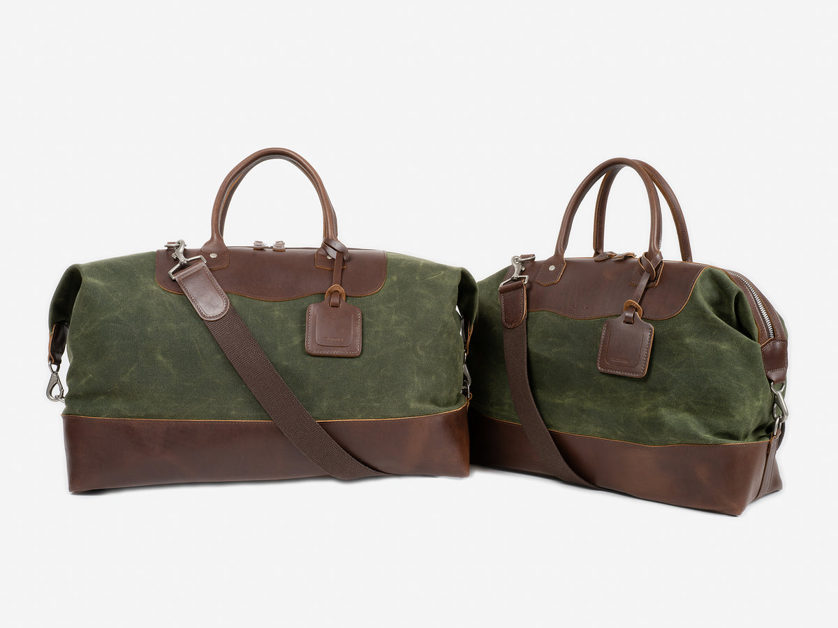 Two green and brown duffel bags with leather accents, handles, shoulder straps, and attached luggage tags, displayed on a white background.