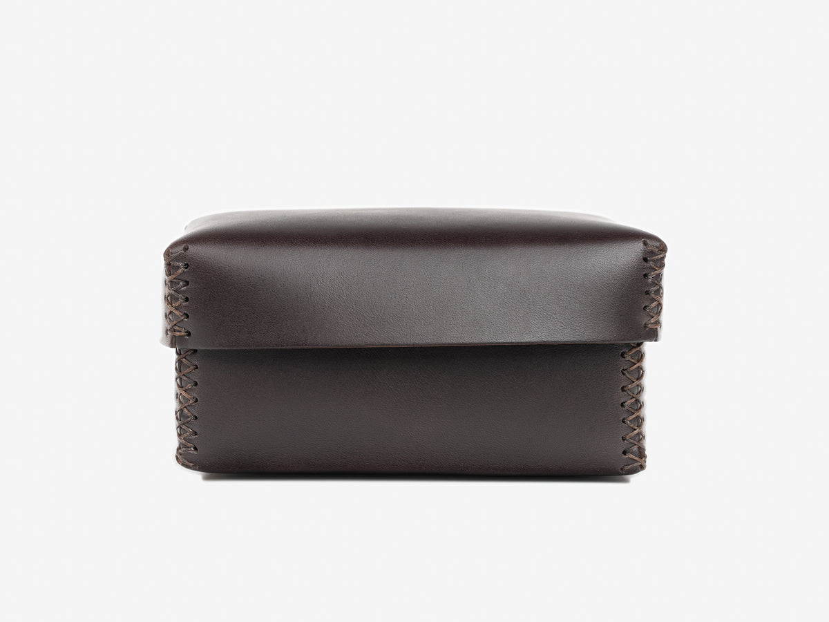 A small, dark brown leather box with visible stitching along the sides, photographed against a plain white background.