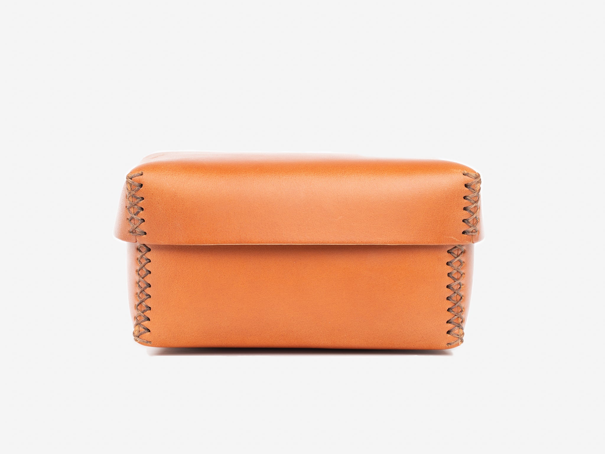A square, tan leather box with visible stitching along the edges, sitting on a plain white background. The lid is closed and the leather appears smooth and glossy.