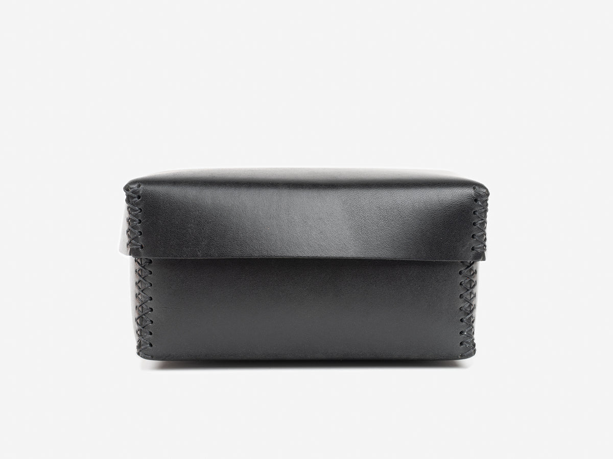 A black rectangular leather box with a flap lid and visible stitching along the edges, set against a plain white background.
