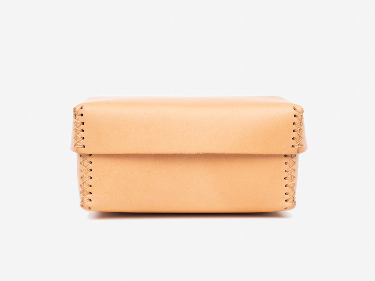 A small, natural leather box with visible stitching along the sides and edges, photographed against a plain white background.