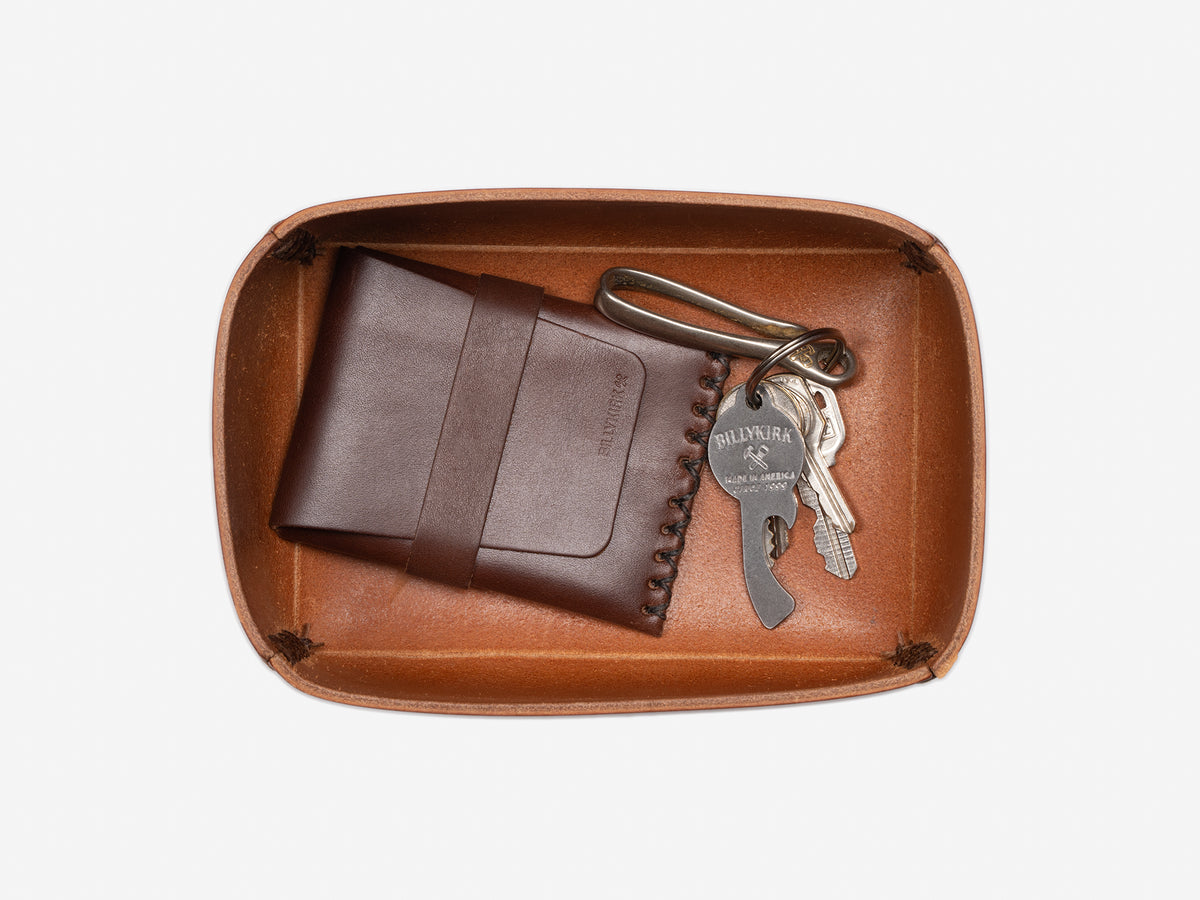 An open tan leather box holding a brown leather wallet and a metal keyring with several keys, all neatly arranged on a white background.