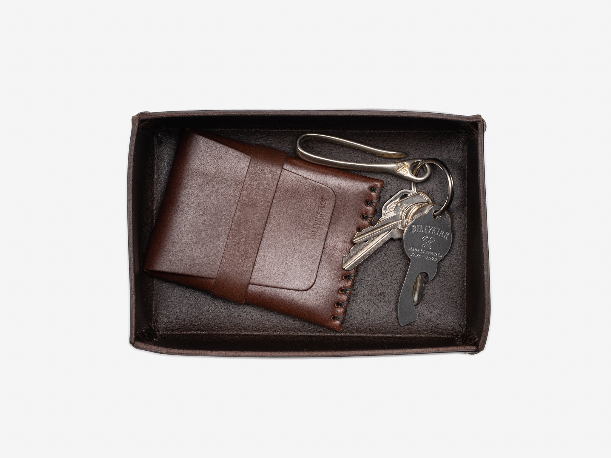 A brown leather wallet and a set of keys with a keychain are neatly placed inside a small, dark brown box on a white background.