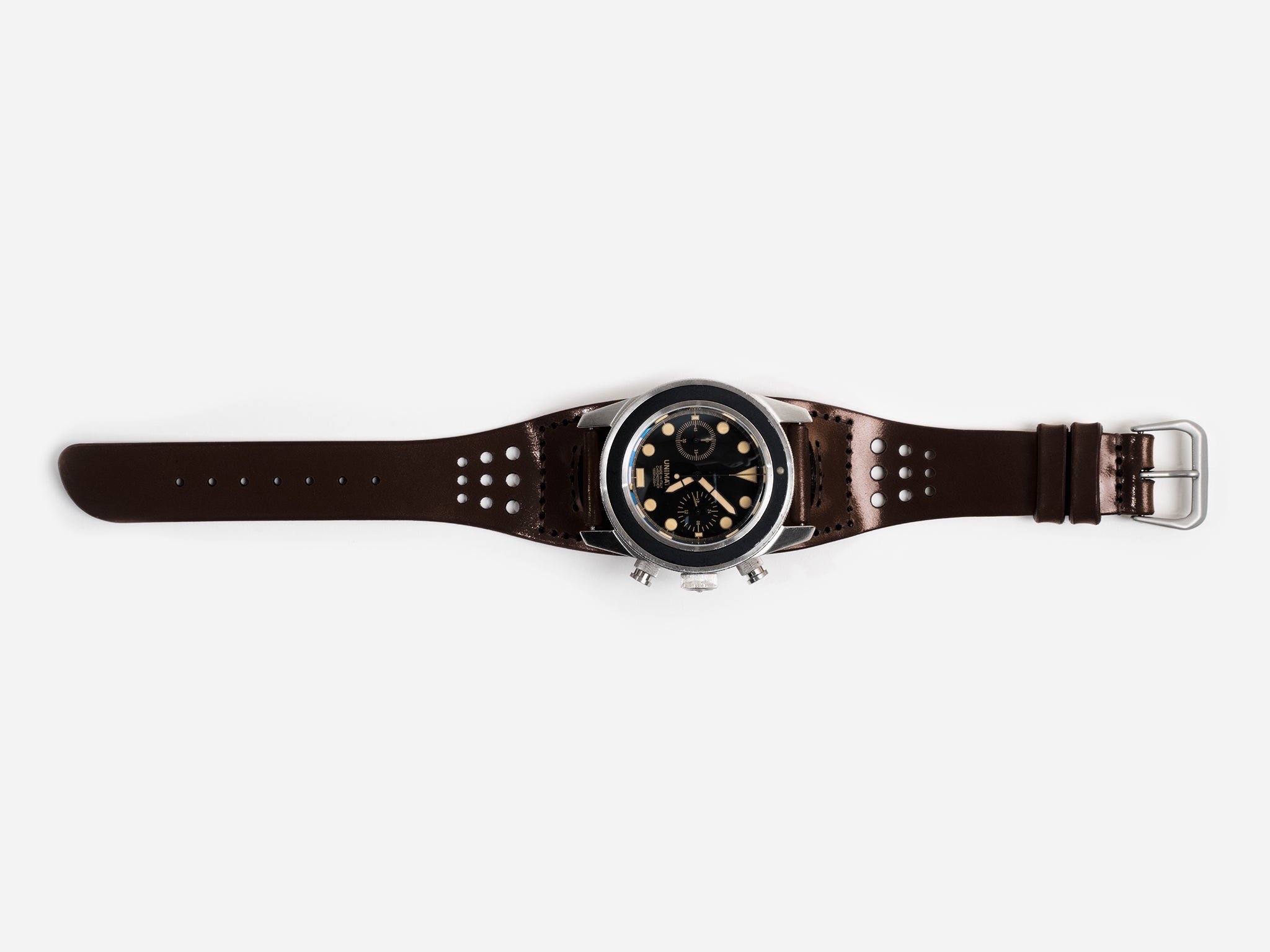 A dark brown cordovan leather watch strap, silver buckle, and a round black dial featuring multiple subdials and gold accents, displayed flat on a white background.