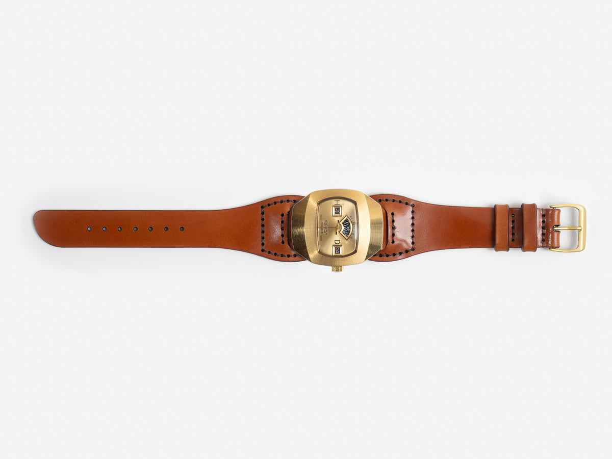 An hourglass-shaped tan cordovan leather strap and a large, brass-toned watch face featuring three small rectangular windows displaying the time digitally.