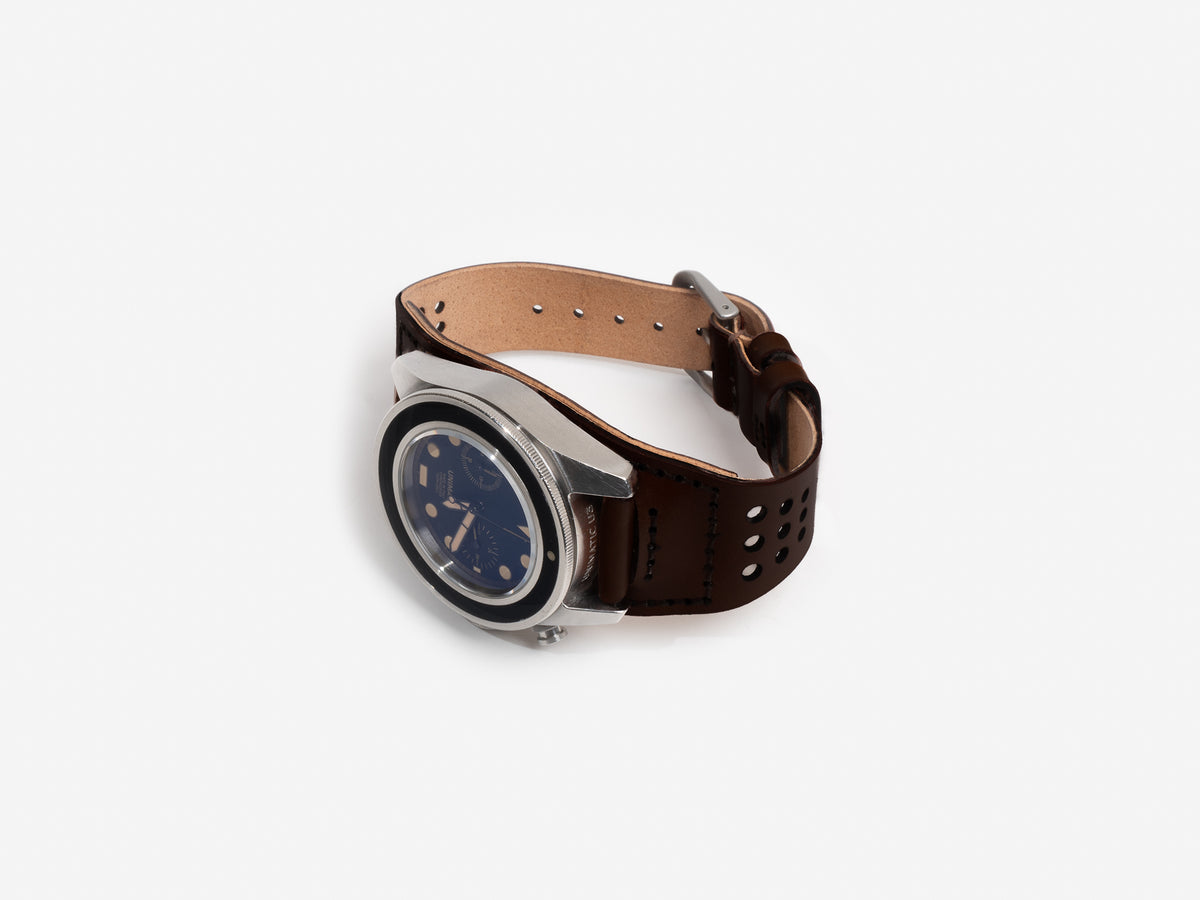 A fastened dark brown cordovan leather watch strap, silver buckle, and a round black dial featuring multiple subdials and gold accents, displayed flat on a white background.