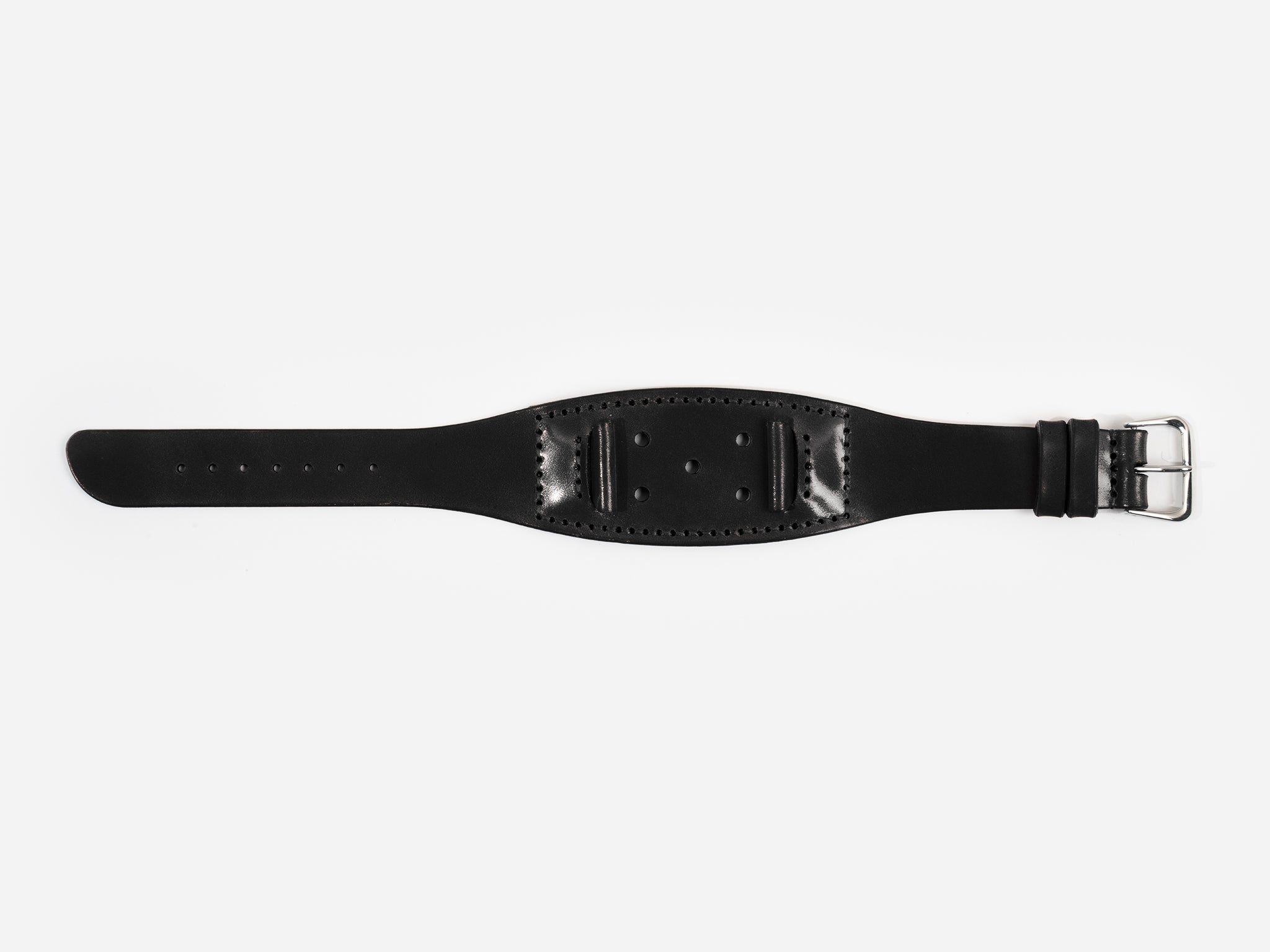 A black cordovan leather watch strap with a silver buckle lies flat on a white background; it has stitched edges and multiple holes for adjustment.