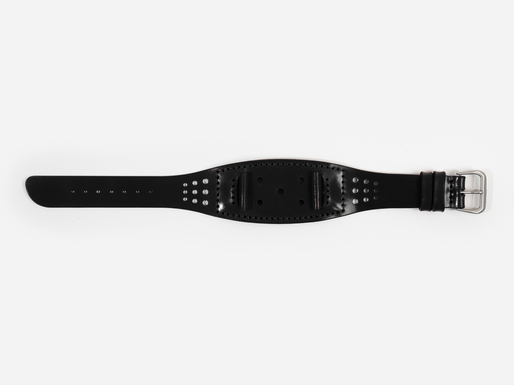 A black cordovan leather watch strap with a silver buckle lies flat on a white background; it has stitched edges and multiple holes for adjustment.