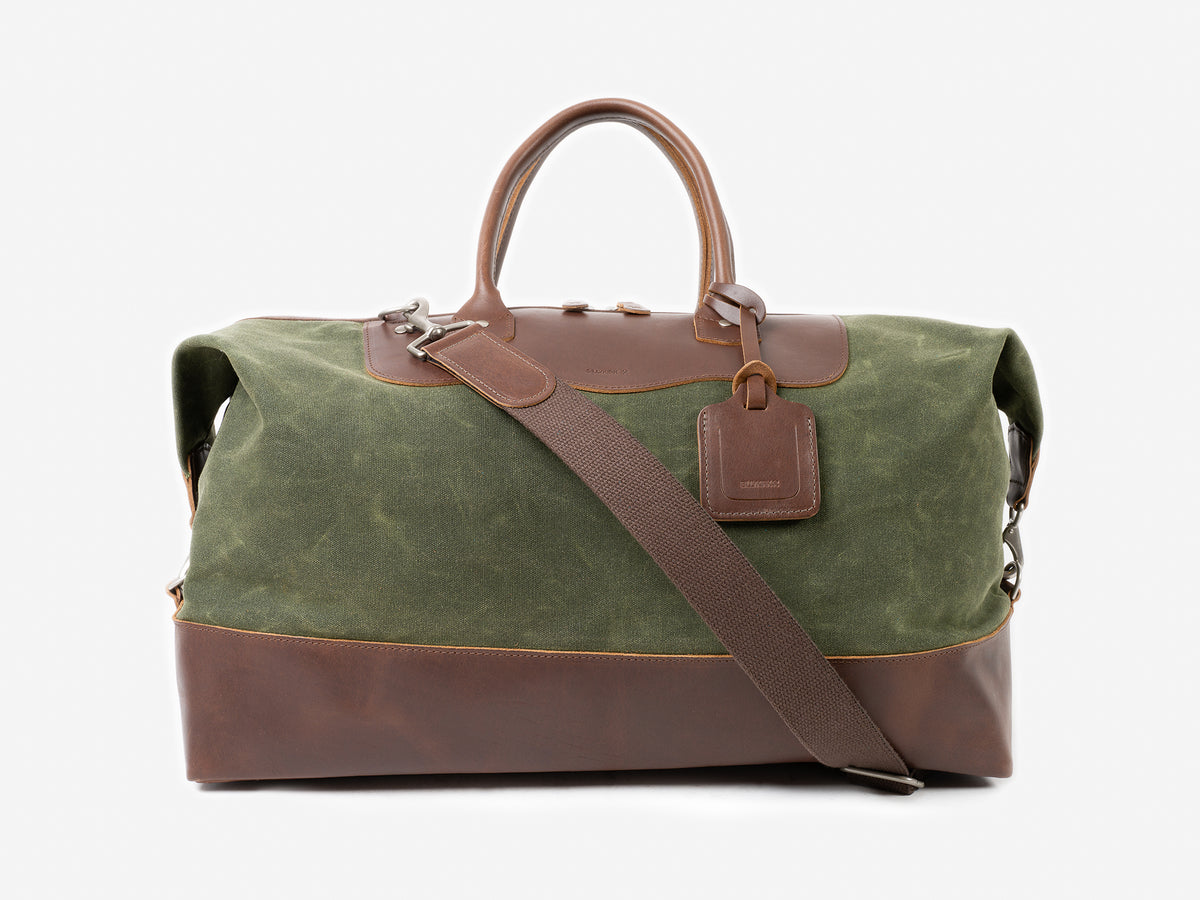 Green and Brown leather duffel bag with a top handle, detachable shoulder strap, and luggage tag, photographed on a plain white background.