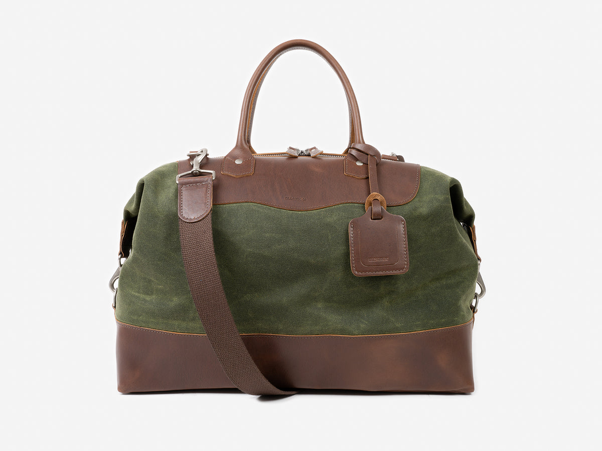 A green and brown leather and canvas duffel bag with two handles, a detachable shoulder strap, and a leather tag, set against a plain white background.