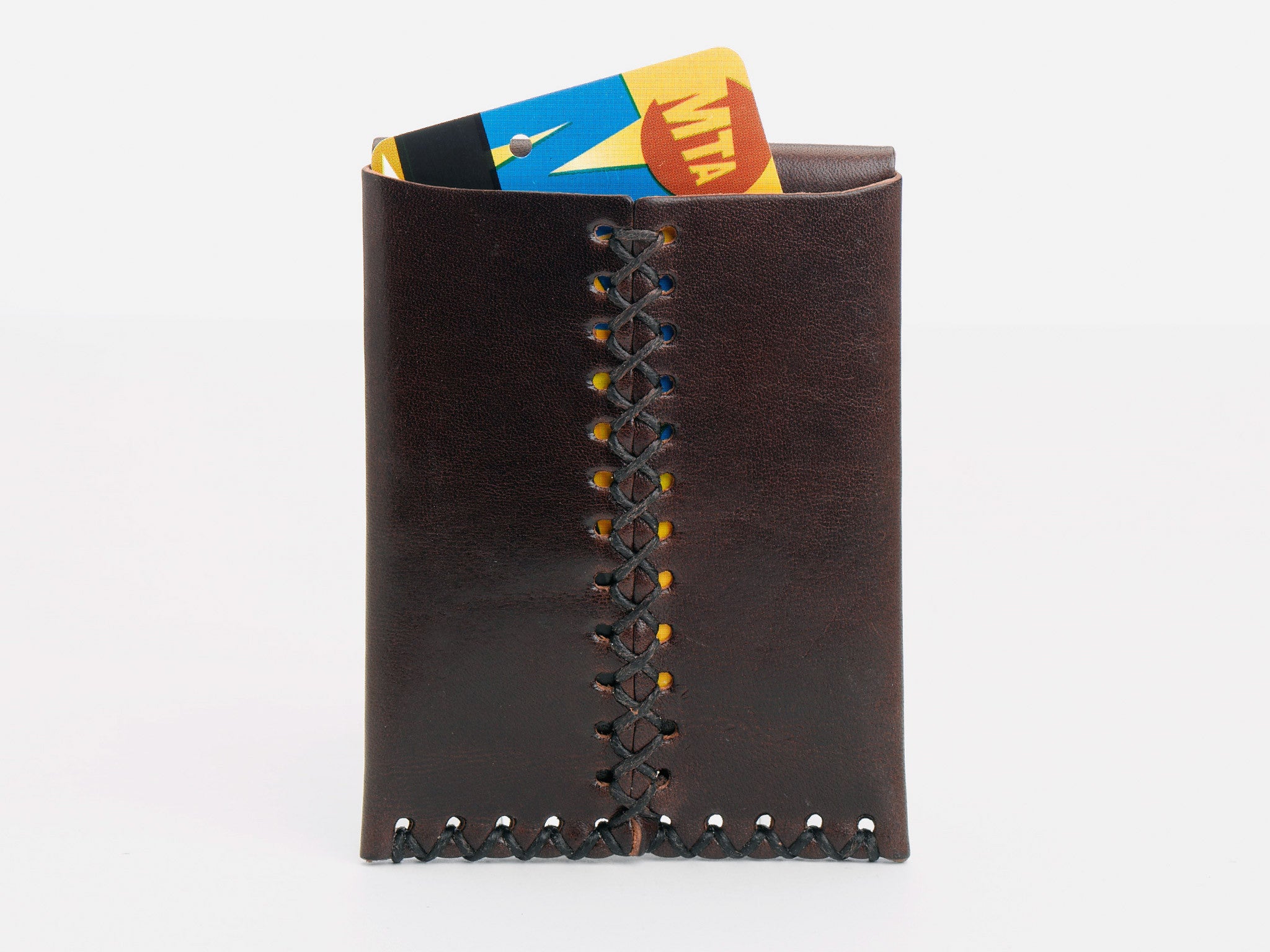 A brown leather wallet with crisscross stitching stands upright, holding a colorful MTA transit card partially visible at the top, against a white background.