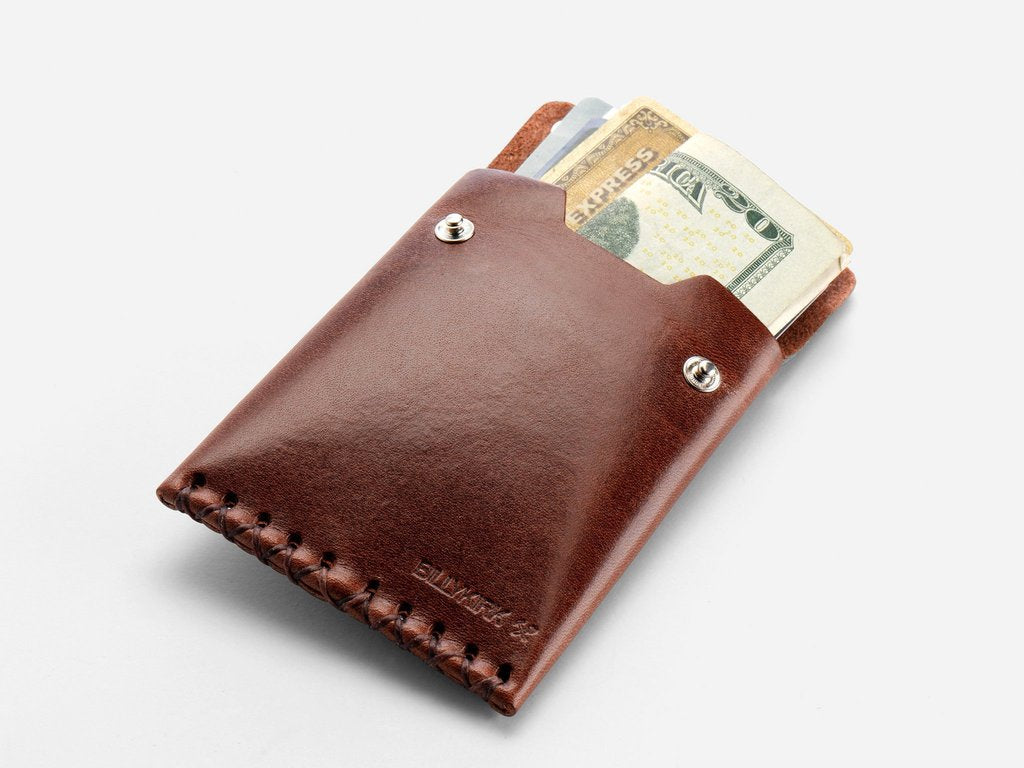 A brown leather wallet with visible stitching holds several credit cards and a folded U.S. twenty-dollar bill, set against a plain white background.