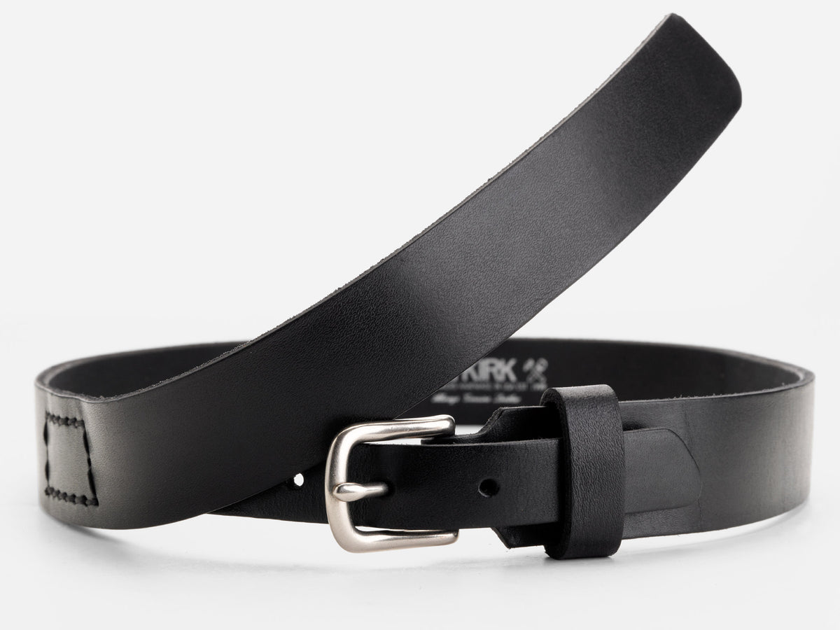 A black leather belt with a silver buckle is curled in a loose loop on a plain white background. The belt has stitched details near the end and a smooth, matte finish.