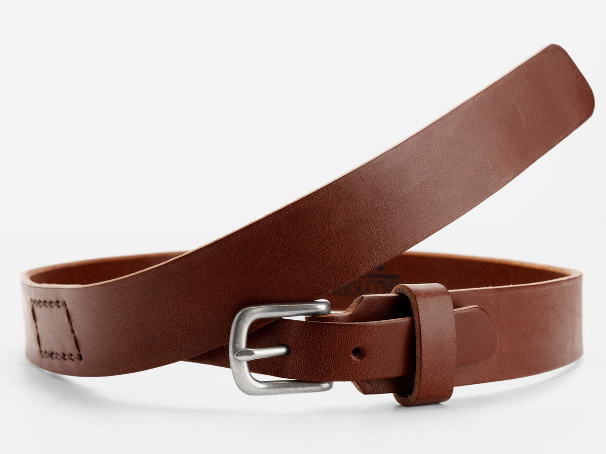 A brown leather belt with a silver buckle is displayed against a white background. The belt is coiled loosely, showing its smooth texture and stitched detail near the end.