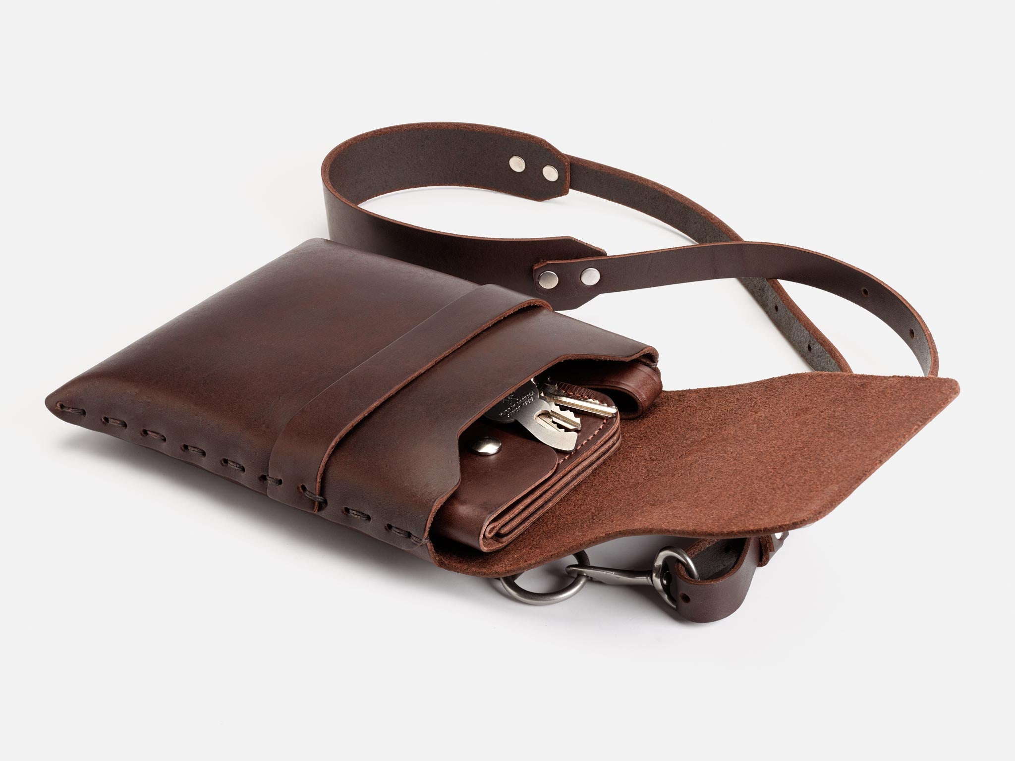 A brown leather crossbody bag with a flap open, revealing a matching leather wallet and a set of keys inside. The bag has a sturdy leather strap and metal hardware, displayed on a white background.