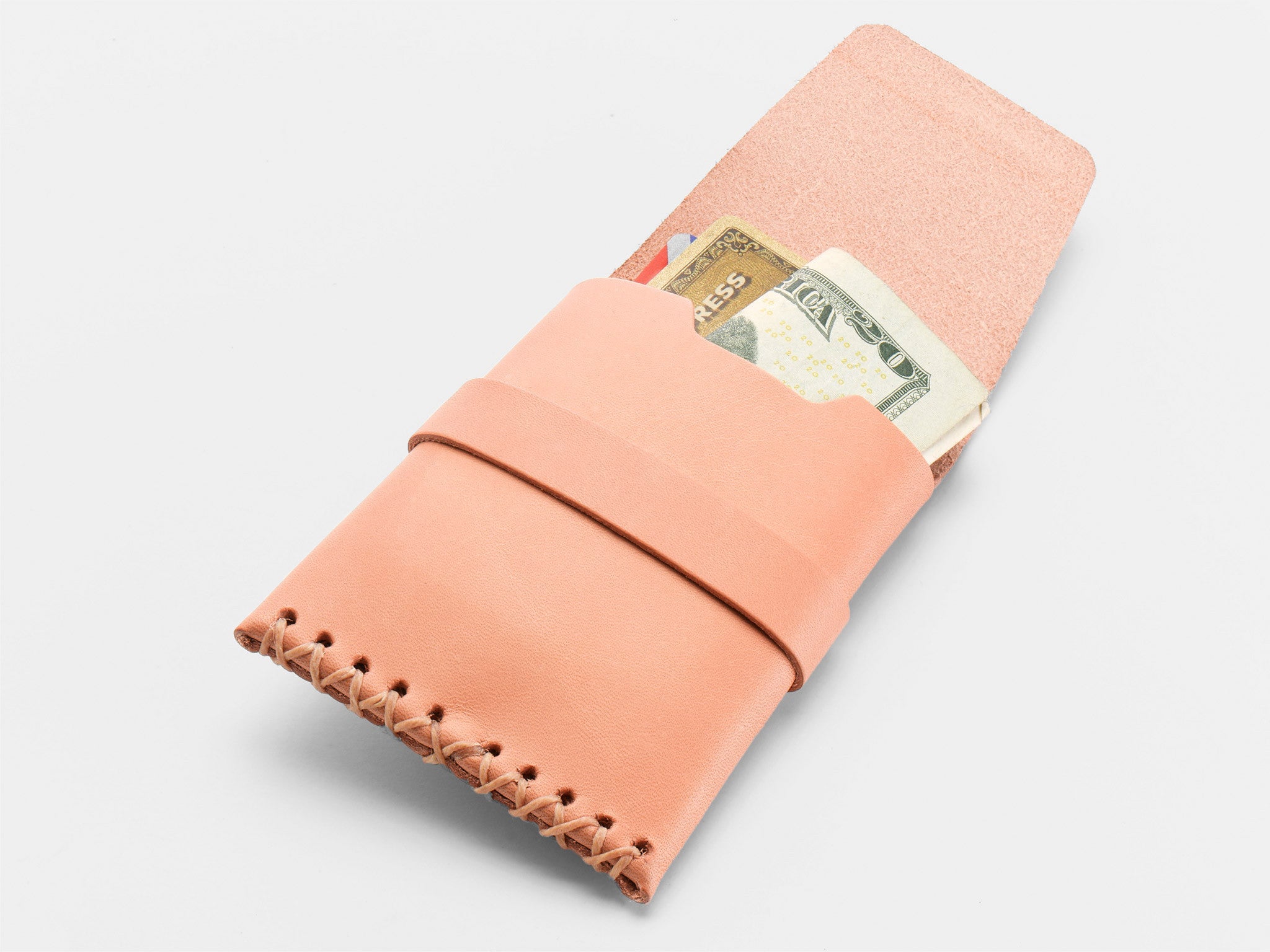 A natural colored leather wallet with visible stitching holds a folded $20 bill, an American Express card, and another credit card, all partially sticking out of the wallet on a white background.