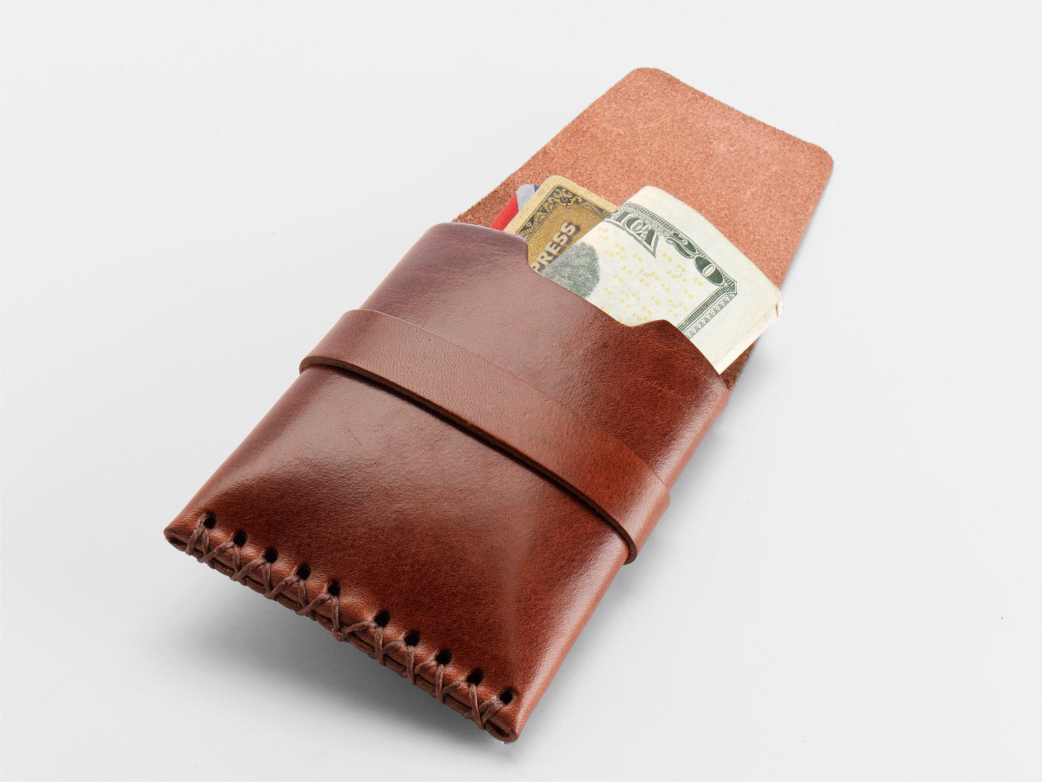 A tan leather wallet with visible stitching holds a folded $20 bill, an American Express card, and another credit card, all partially sticking out of the wallet on a white background.