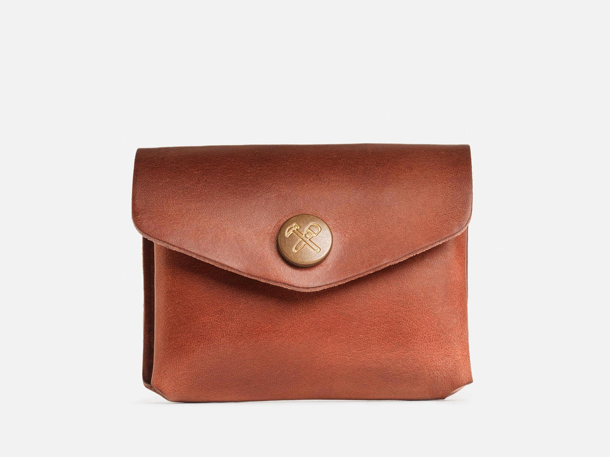 A closed tan coin pouch with a brass snap featuring a hammer and maul logo