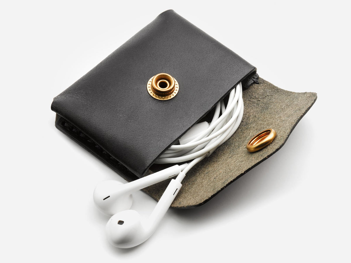 A black leather coin pouch with a brass snap closure, partially opened to show white earphones inside.