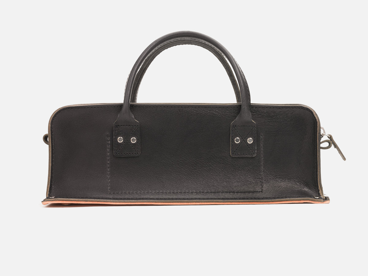 A back view of a black leather tool bag with rivet reinforced corners and handles set in a white background