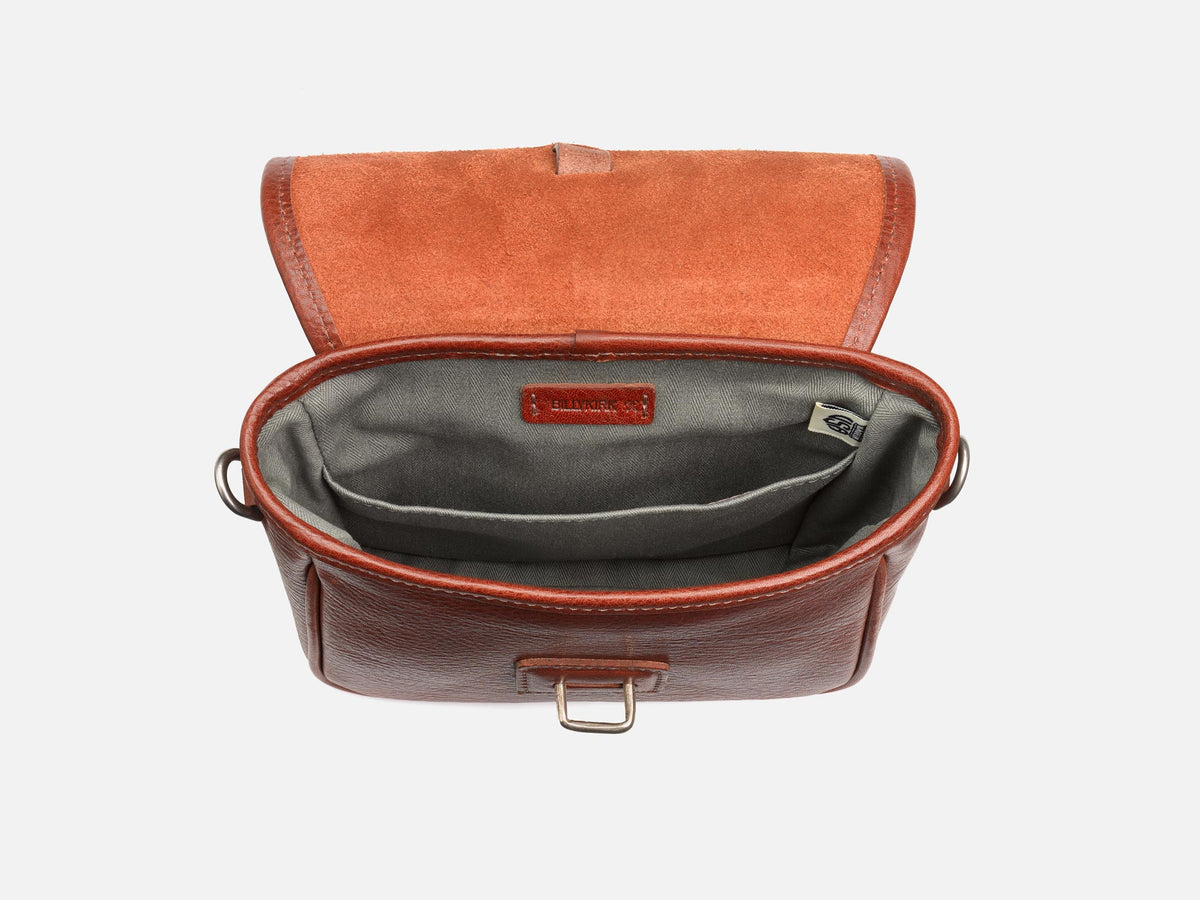 A brown leather bag with the top flap open, revealing a gray fabric-lined interior with two inner pockets and a visible label inside. The bag is positioned against a plain white background.