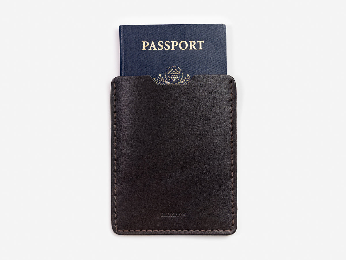 A dark brown leather passport holder with a navy blue passport partially visible inside, both placed against a plain white background.